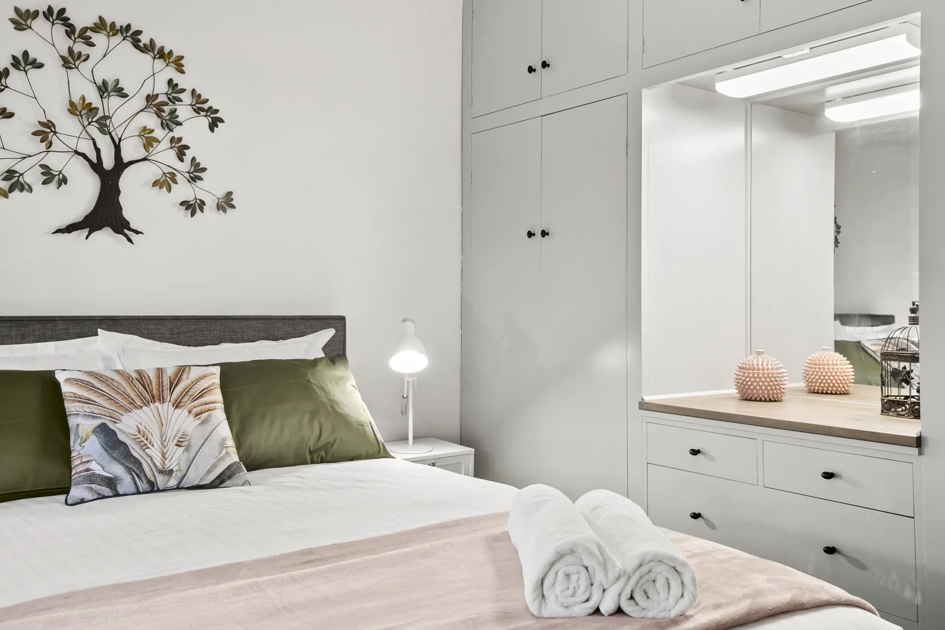 A white, modern bedroom with a bed, wardrobe, and a tree wall accent.