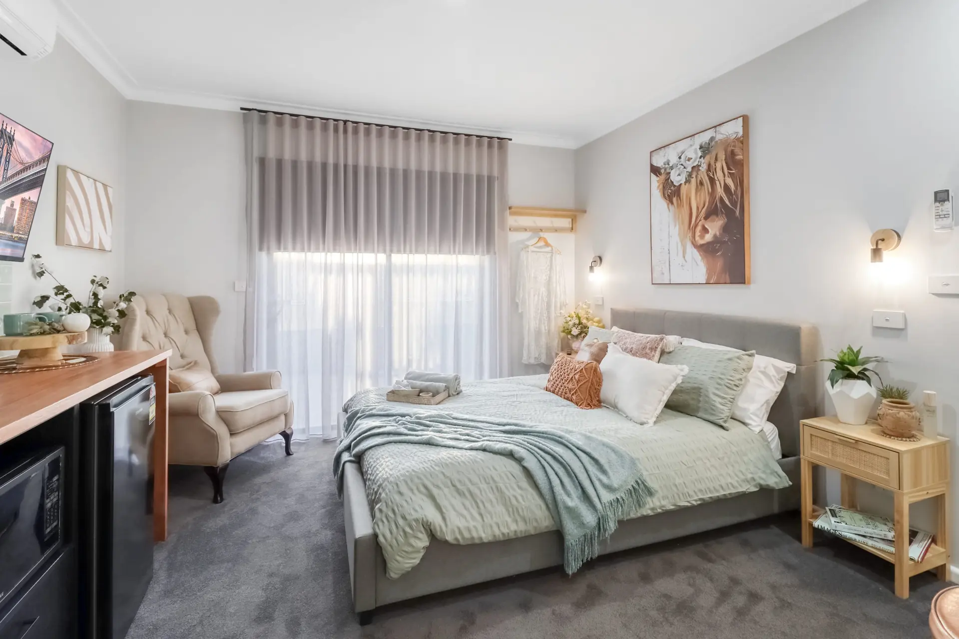 A bedroom with a bed, armchair, and mini-fridge.