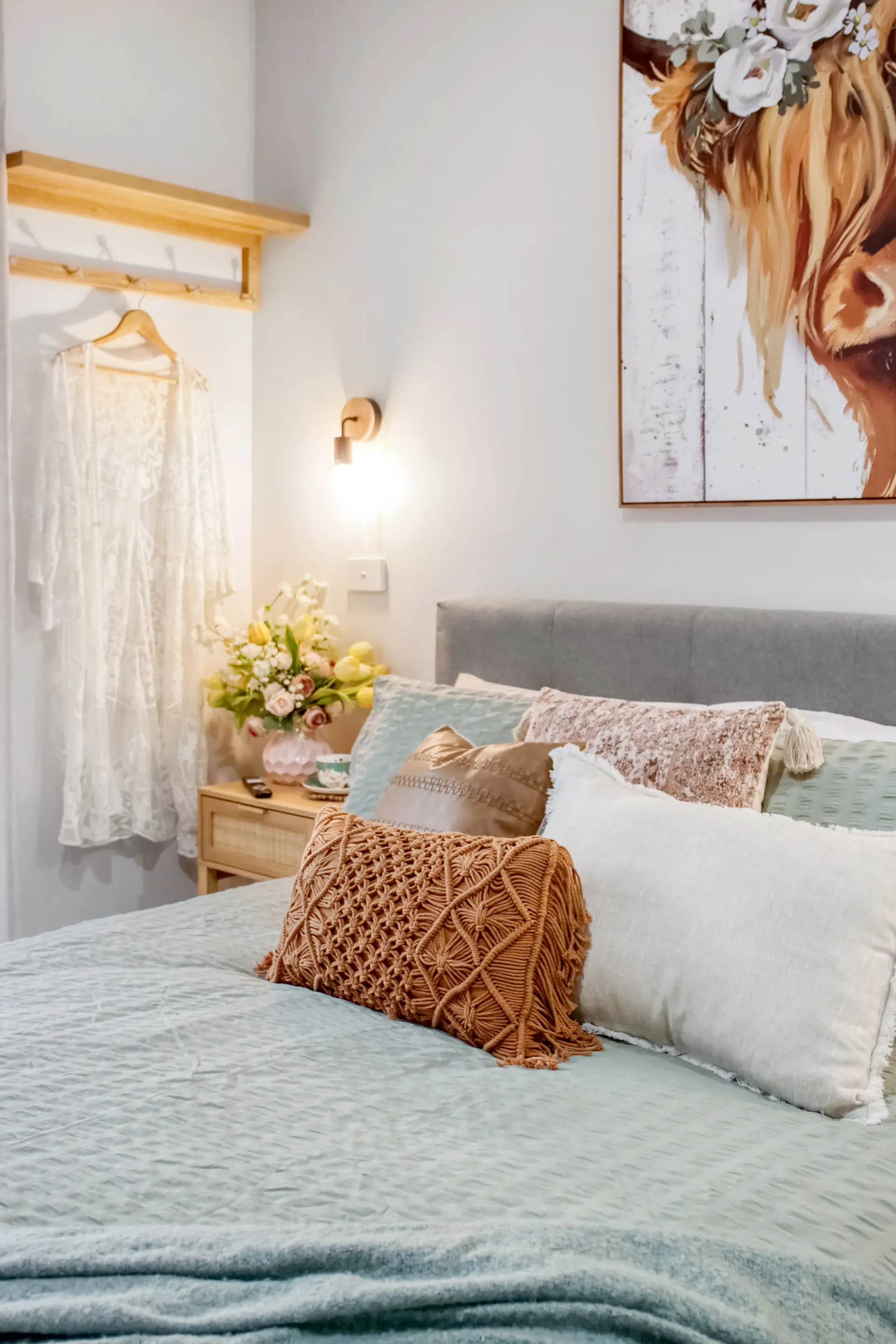 A bed with light blue bedding, decorative pillows, and a painting of a cow.