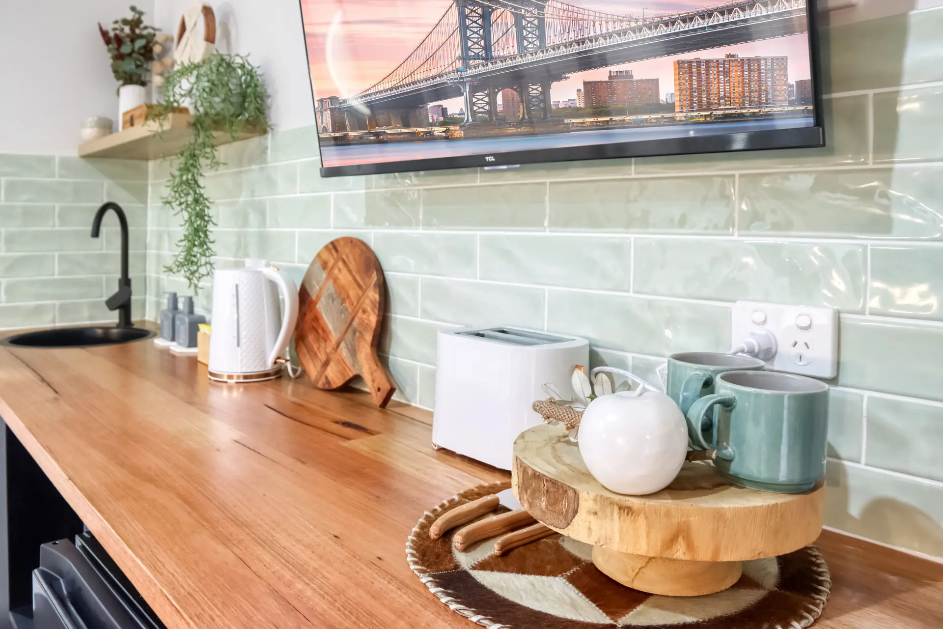 A kitchen counter with a sink, toaster, mugs, and a cutting board.