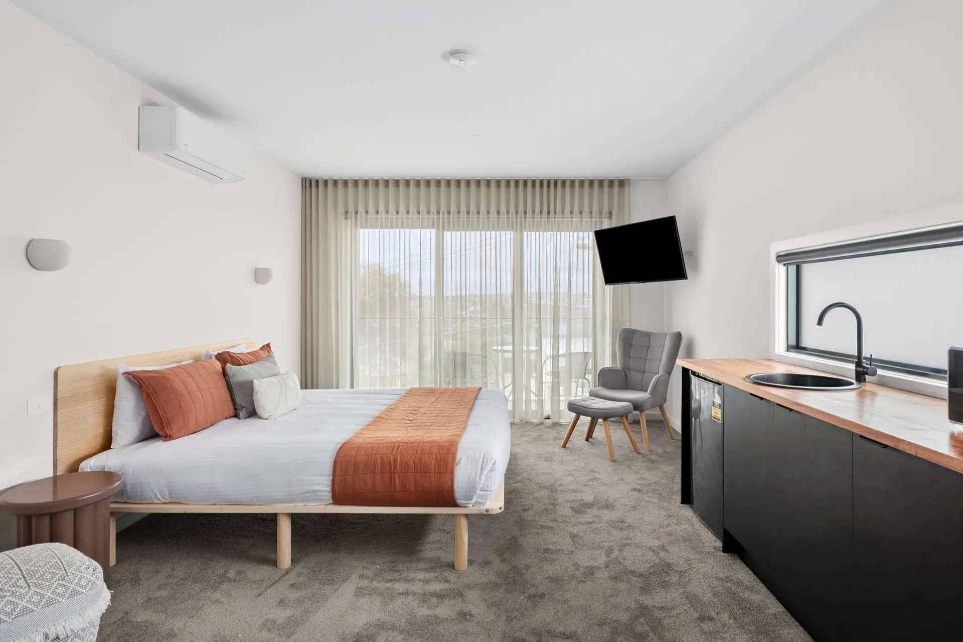 A modern studio hotel room with a bed, kitchenette, and seating area.