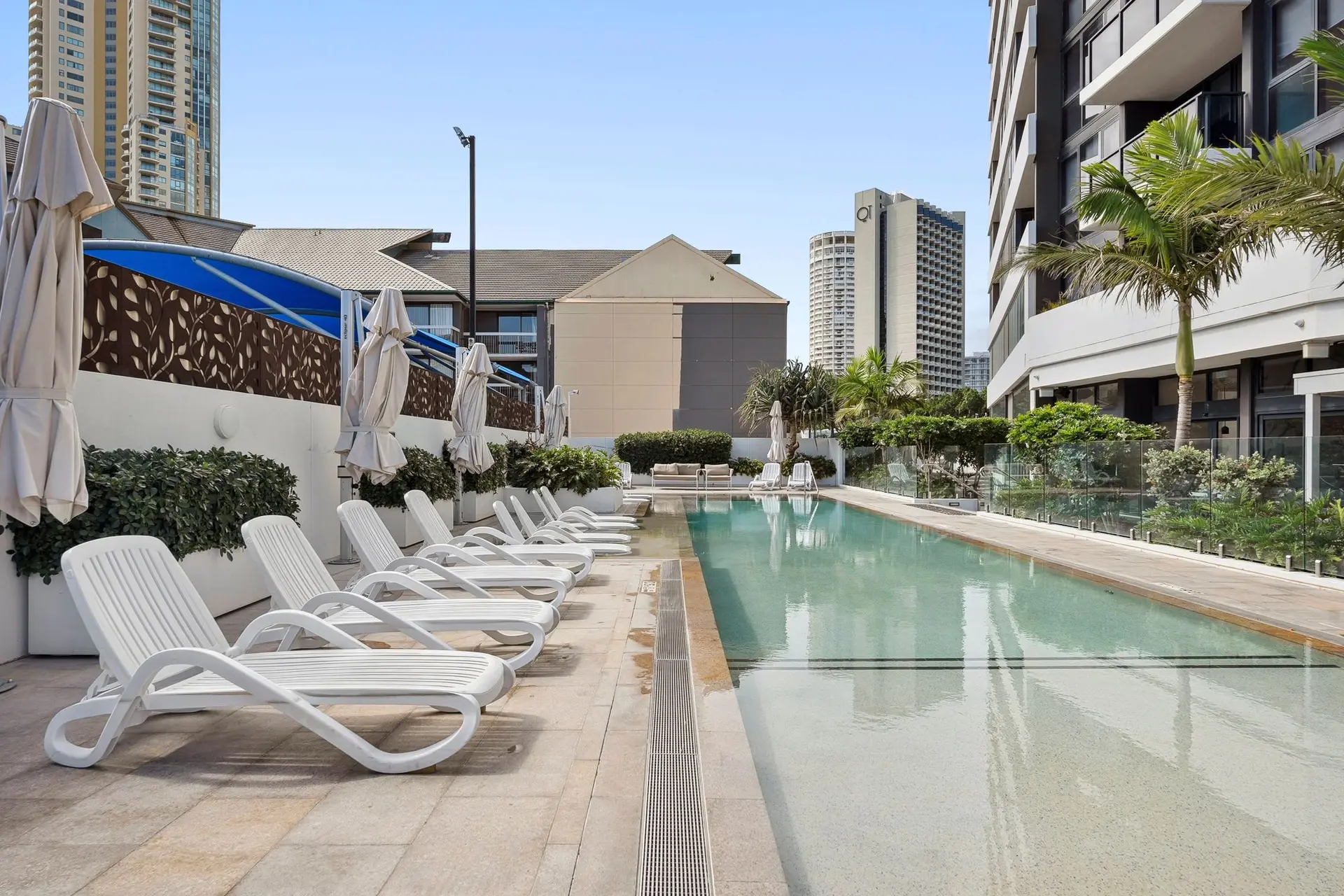White lounge chairs line the edge of a bright blue swimming pool.