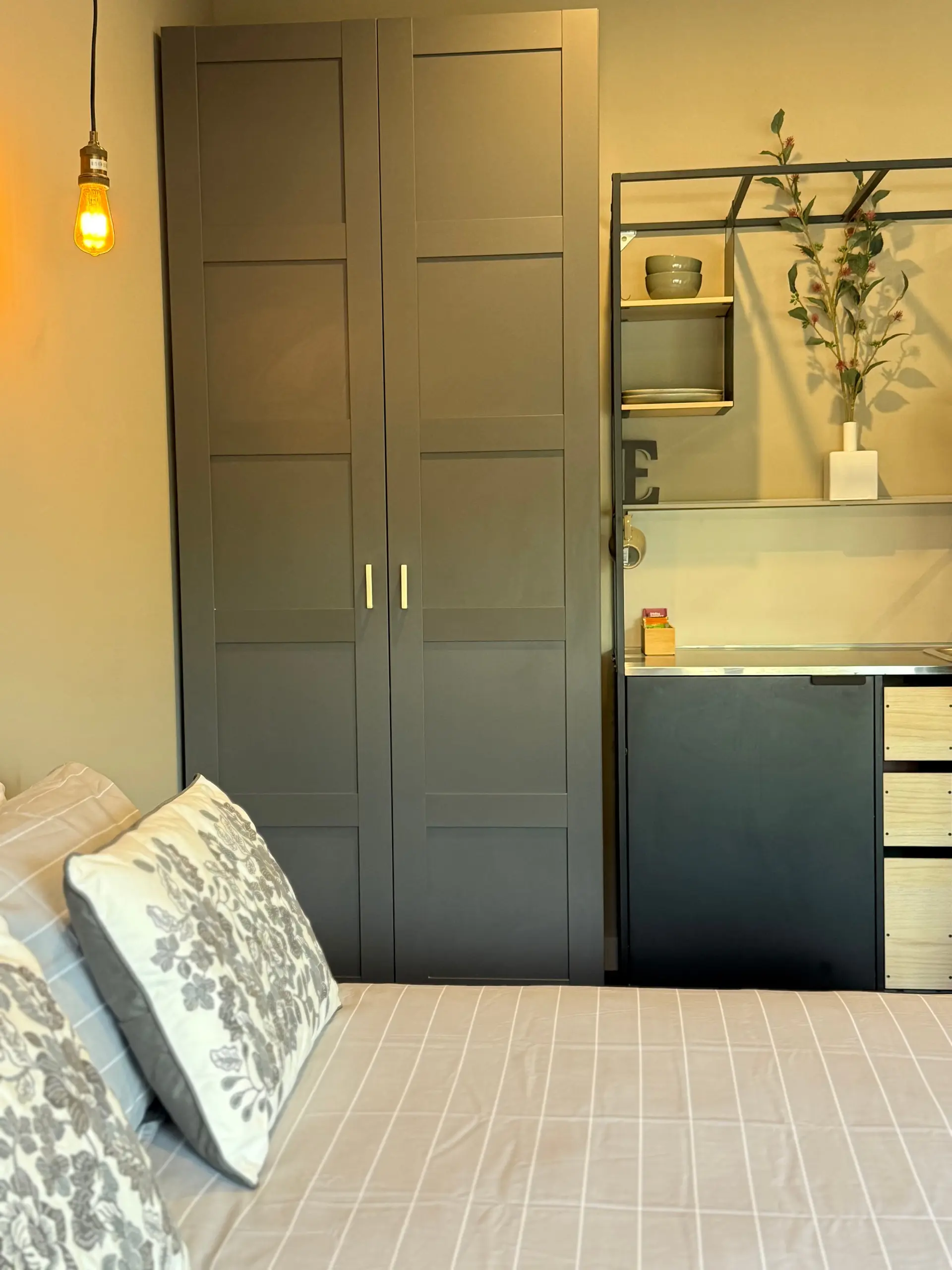 A bedroom scene featuring pillows, a bed, a wardrobe, and shelving with decor.