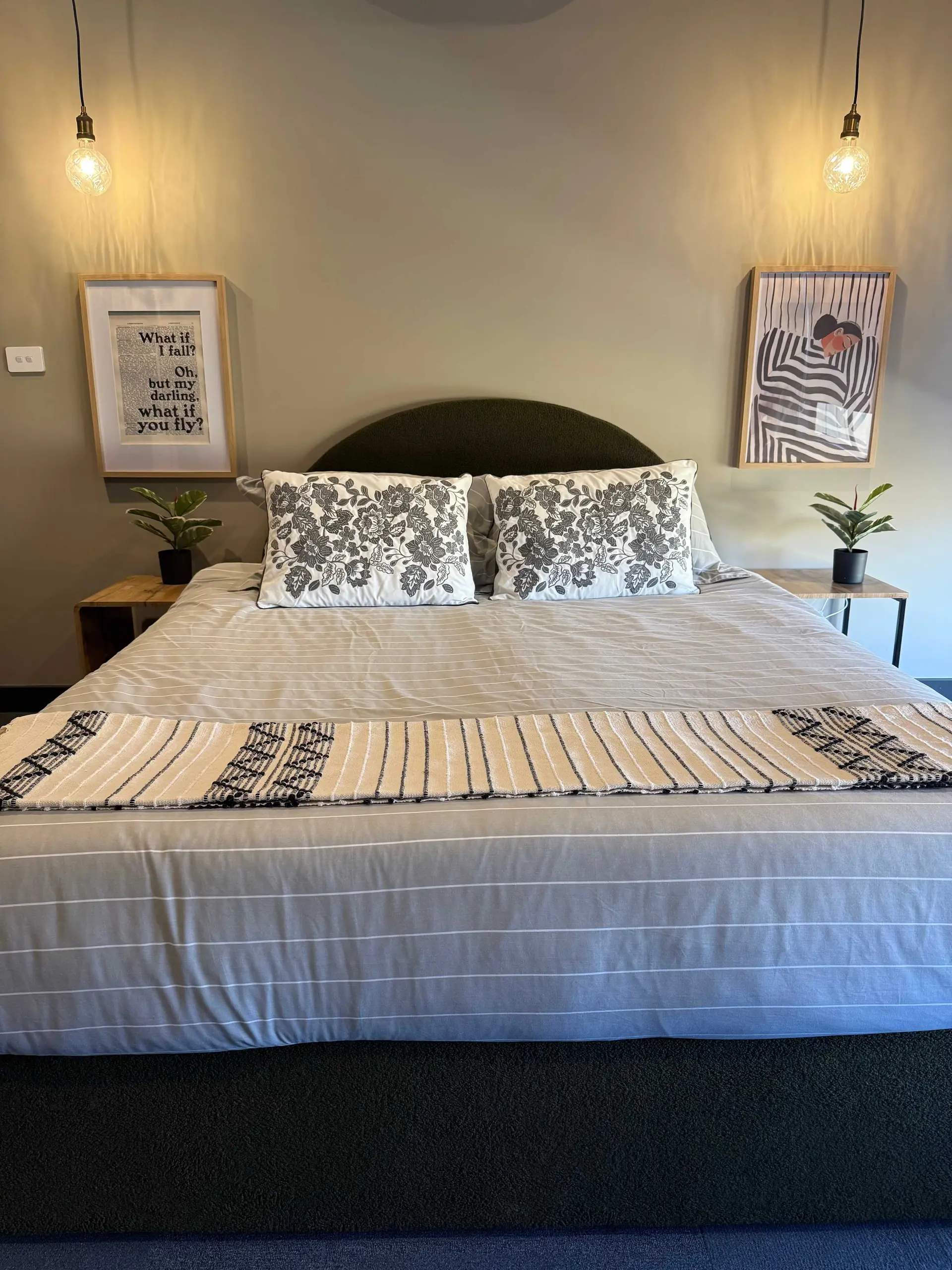 A bedroom with a bed, pillows, artwork, and a plant.