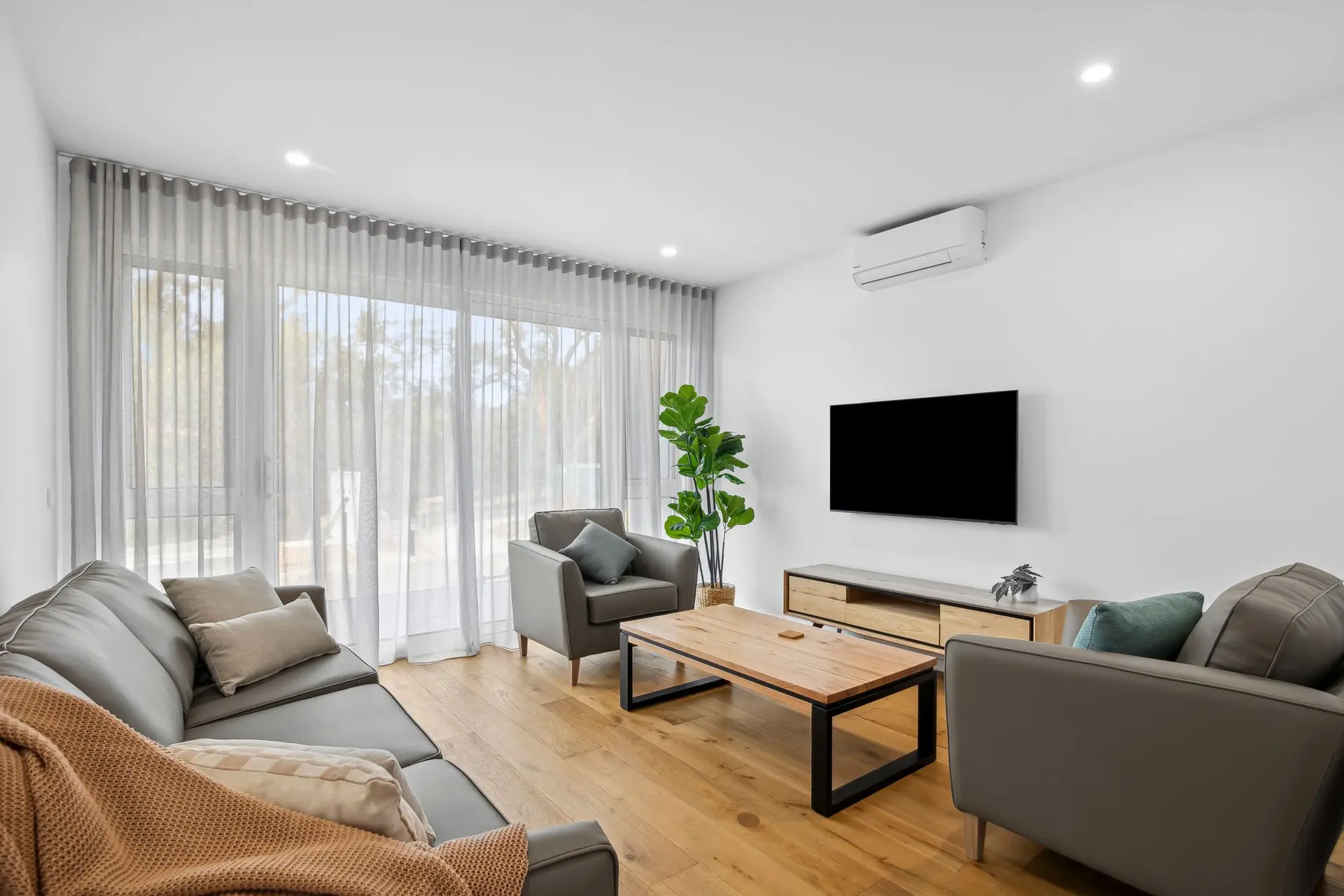 Living room with grey sectional sofa, armchair, coffee table, TV, and large windows with sheer curta