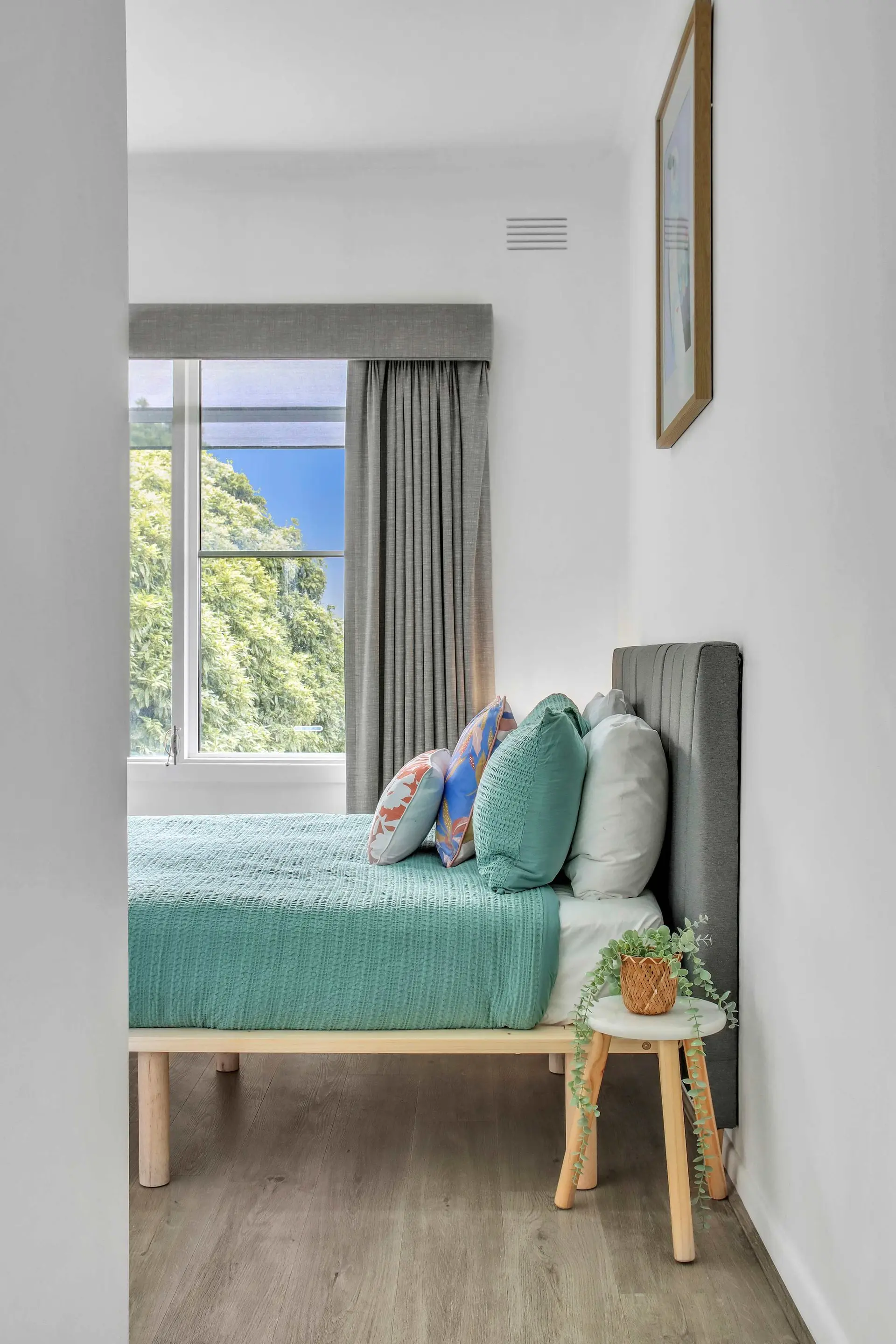 Bedroom with a bed, pillows, and a window with greenery outside.
