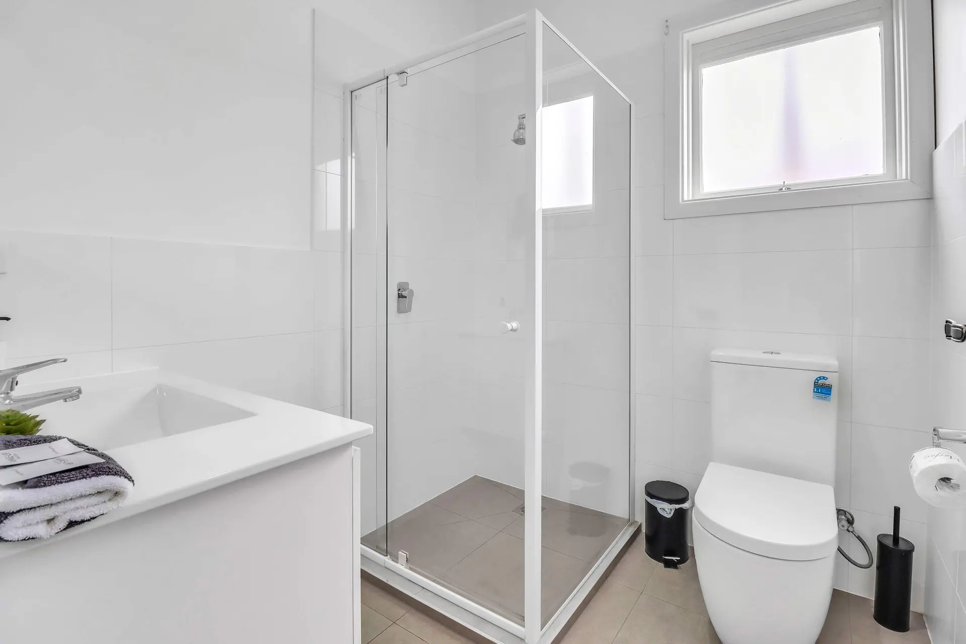 A clean, modern white bathroom with a glass-enclosed shower, toilet, and sink.