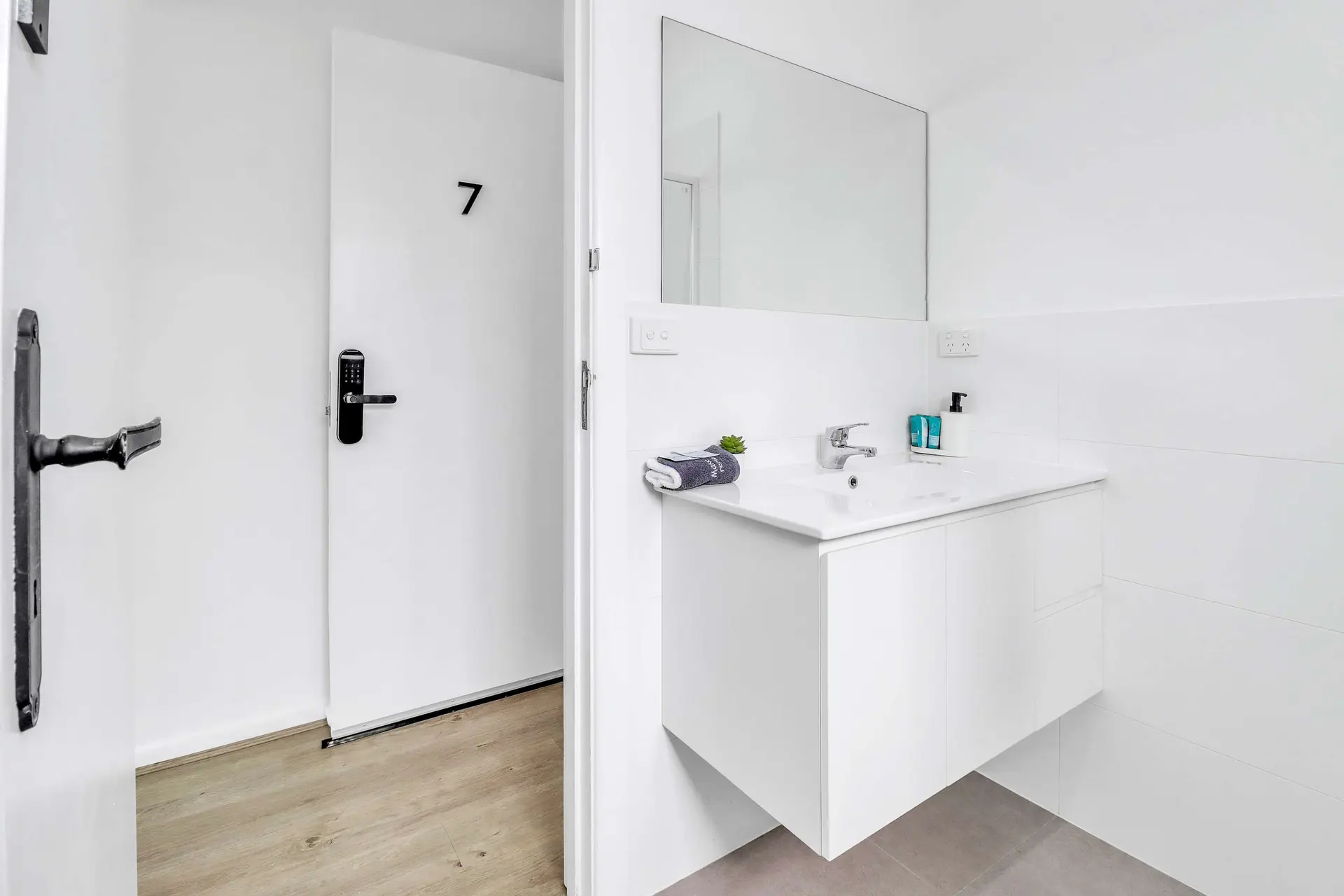 A modern bathroom with a white vanity, sink, and mirror, plus a door with a digital lock.