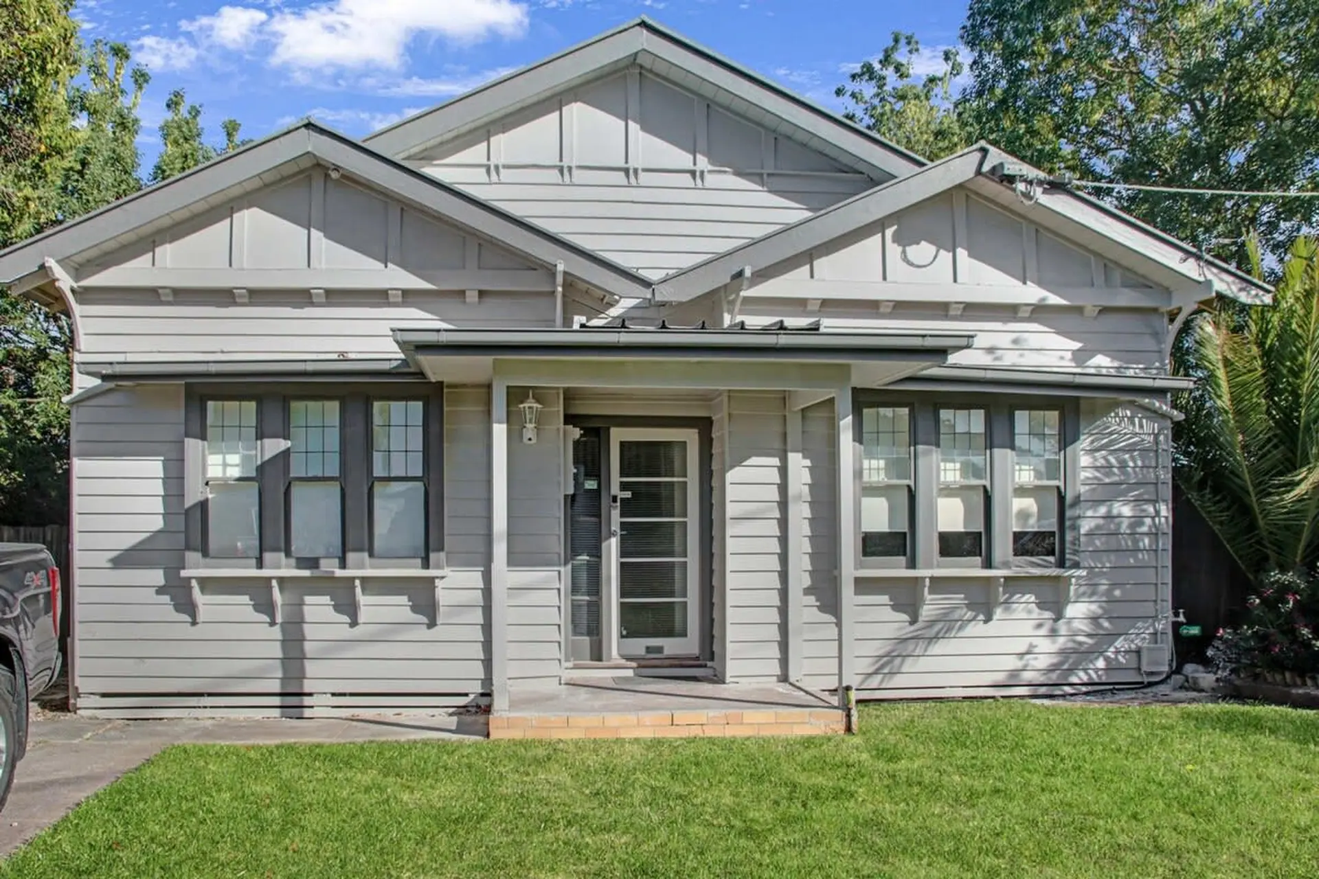 A gray-sided bungalow with white trim, a covered porch with a glass door, and manicured green lawn.