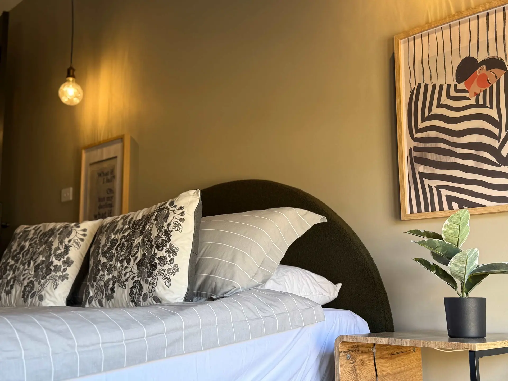 A bed with pillows and a framed artwork above a potted plant.