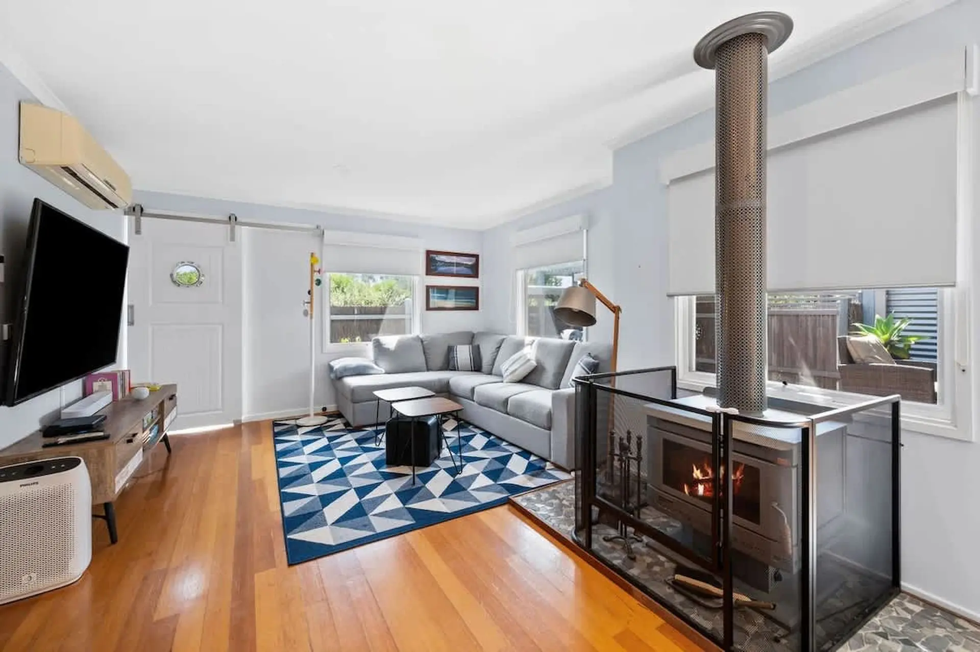A modern living room with a grey sectional sofa, a wood-burning stove, and a flat-screen TV.