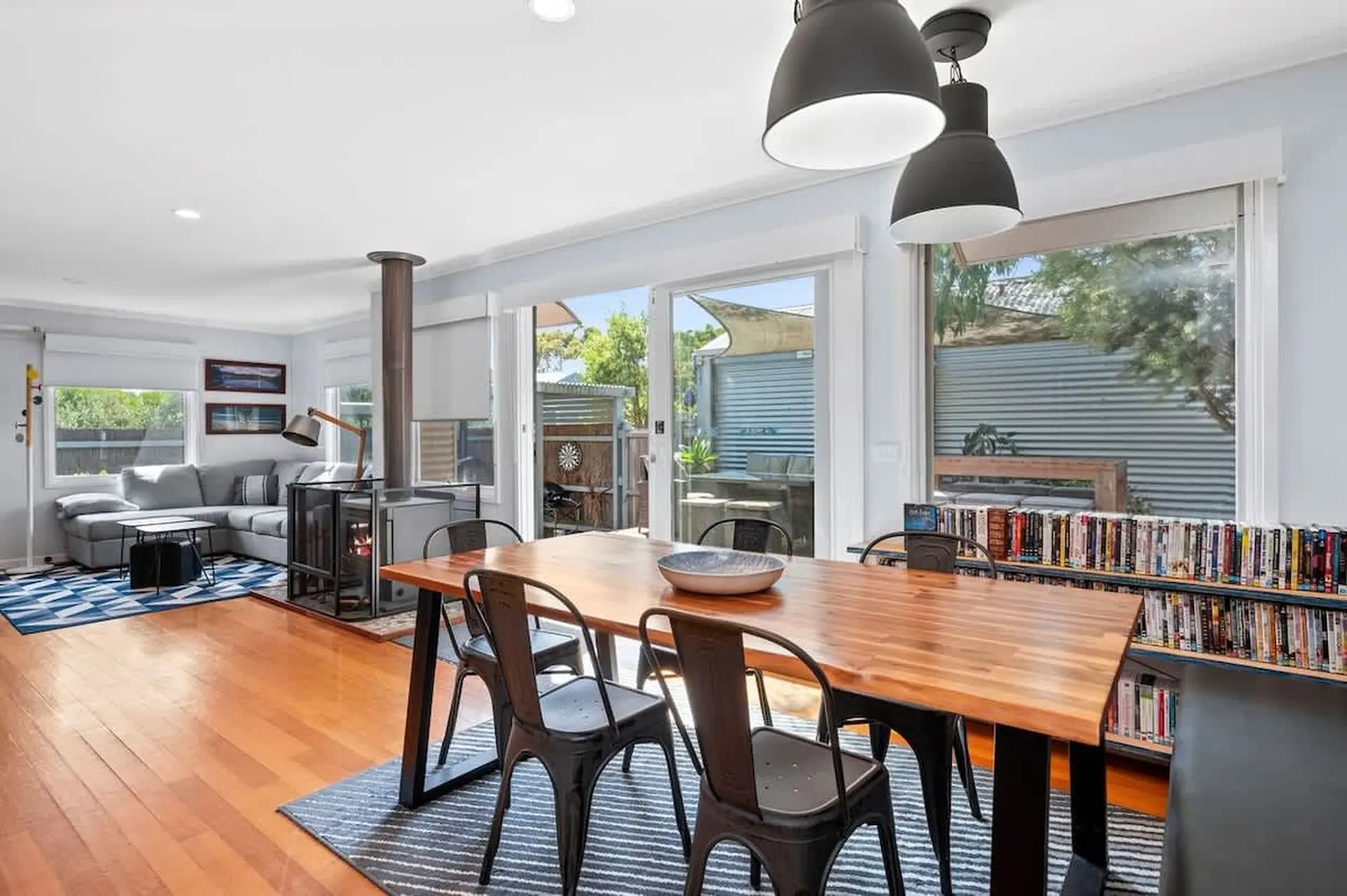 A dining table with chairs sits in front of a window with a view of a backyard.