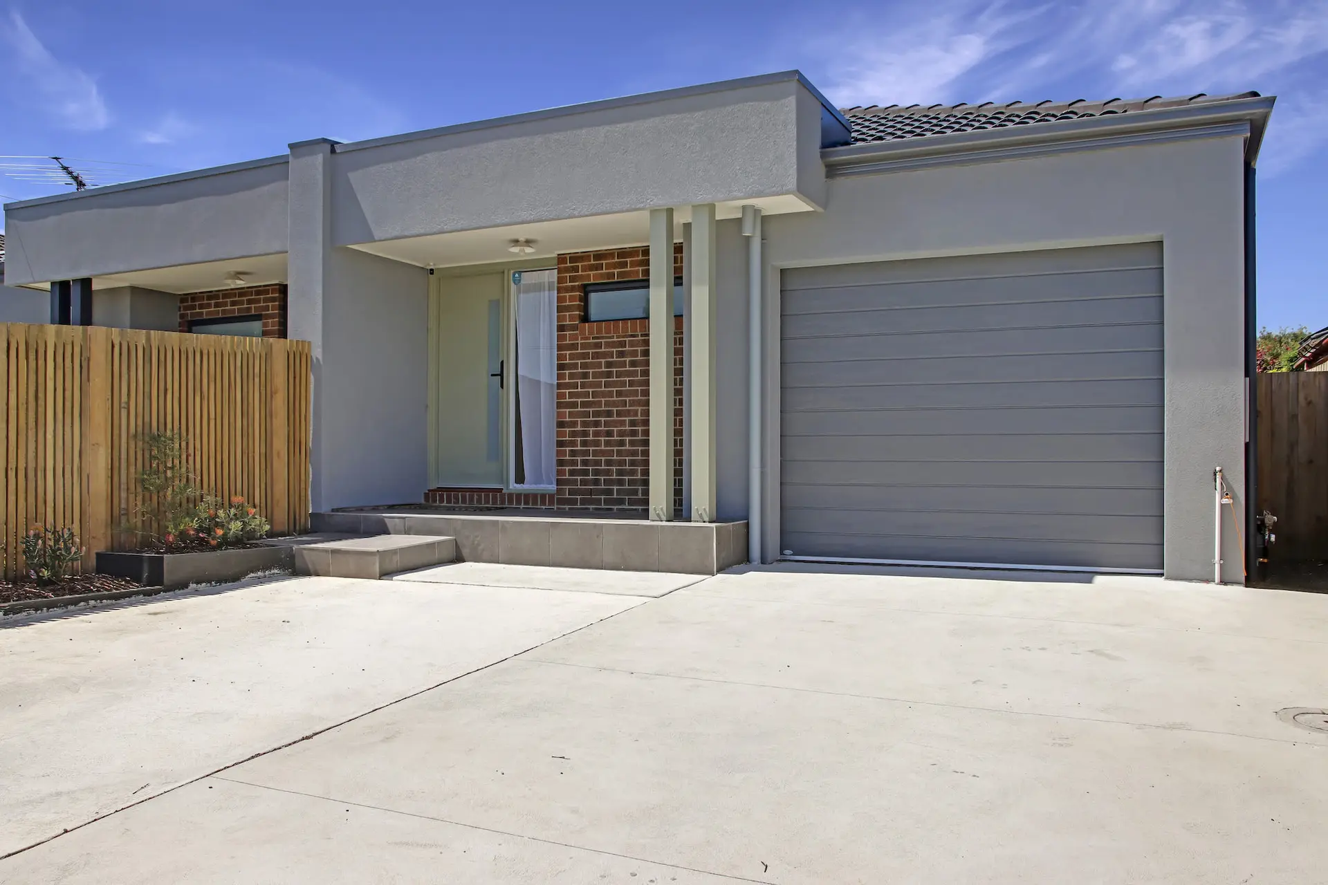Modern house with gray garage door, brick facade, and wooden fence.