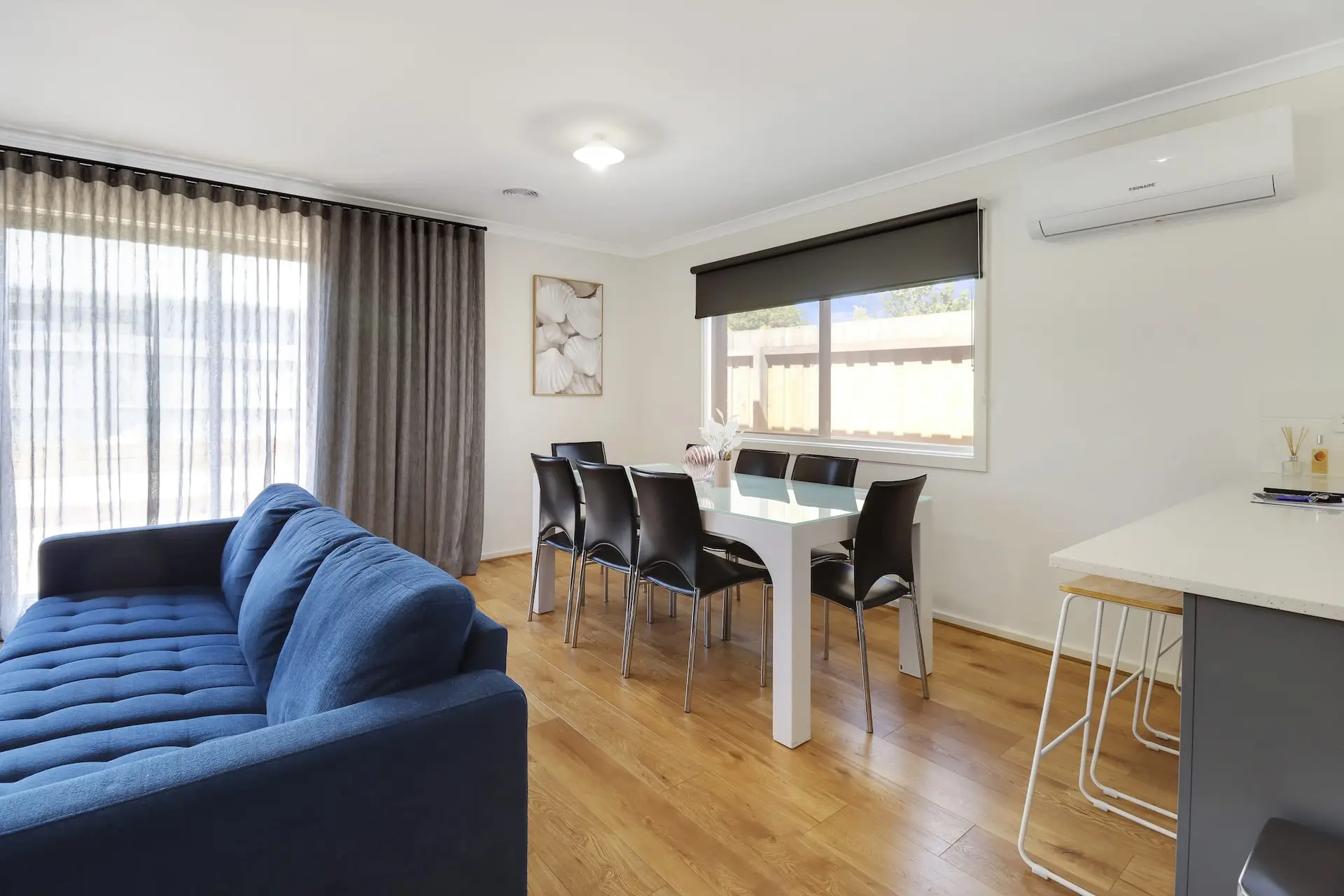 A modern living and dining area with a blue couch, white dining table, and black chairs.