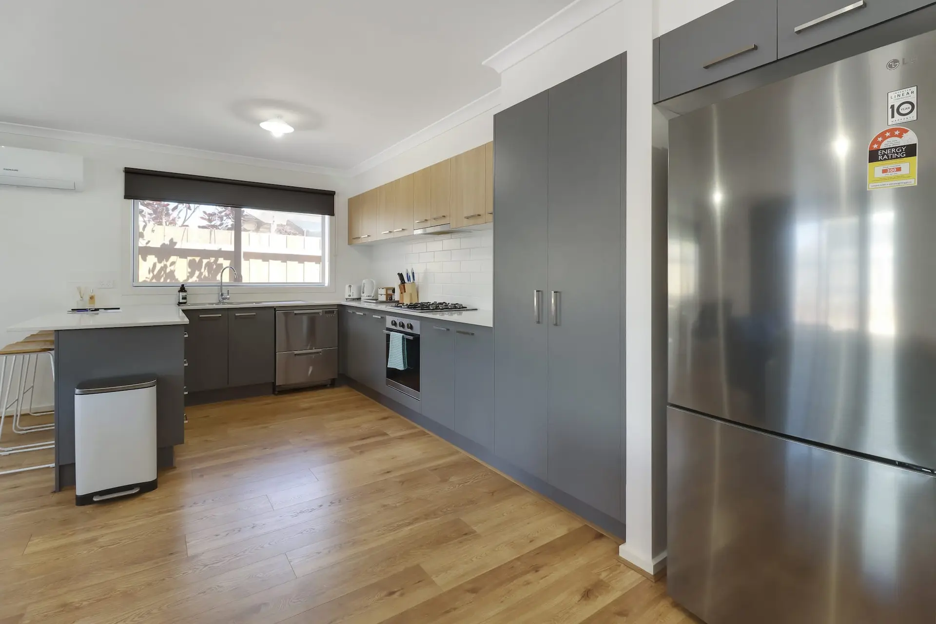 A modern kitchen with stainless steel appliances, grey cabinets, and wood floors.
