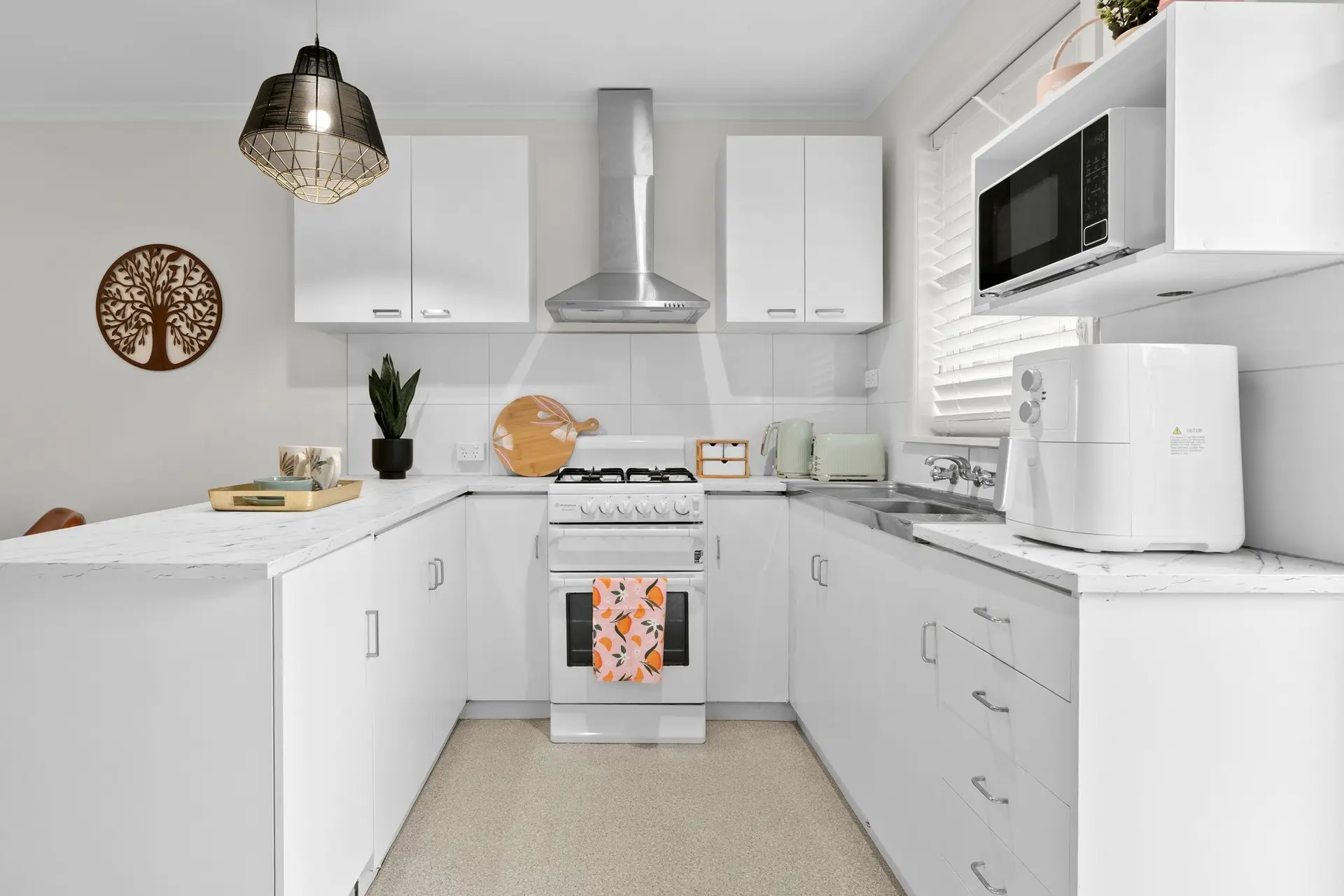 A modern kitchen features white cabinets, a gas stove, and a sleek vent hood.