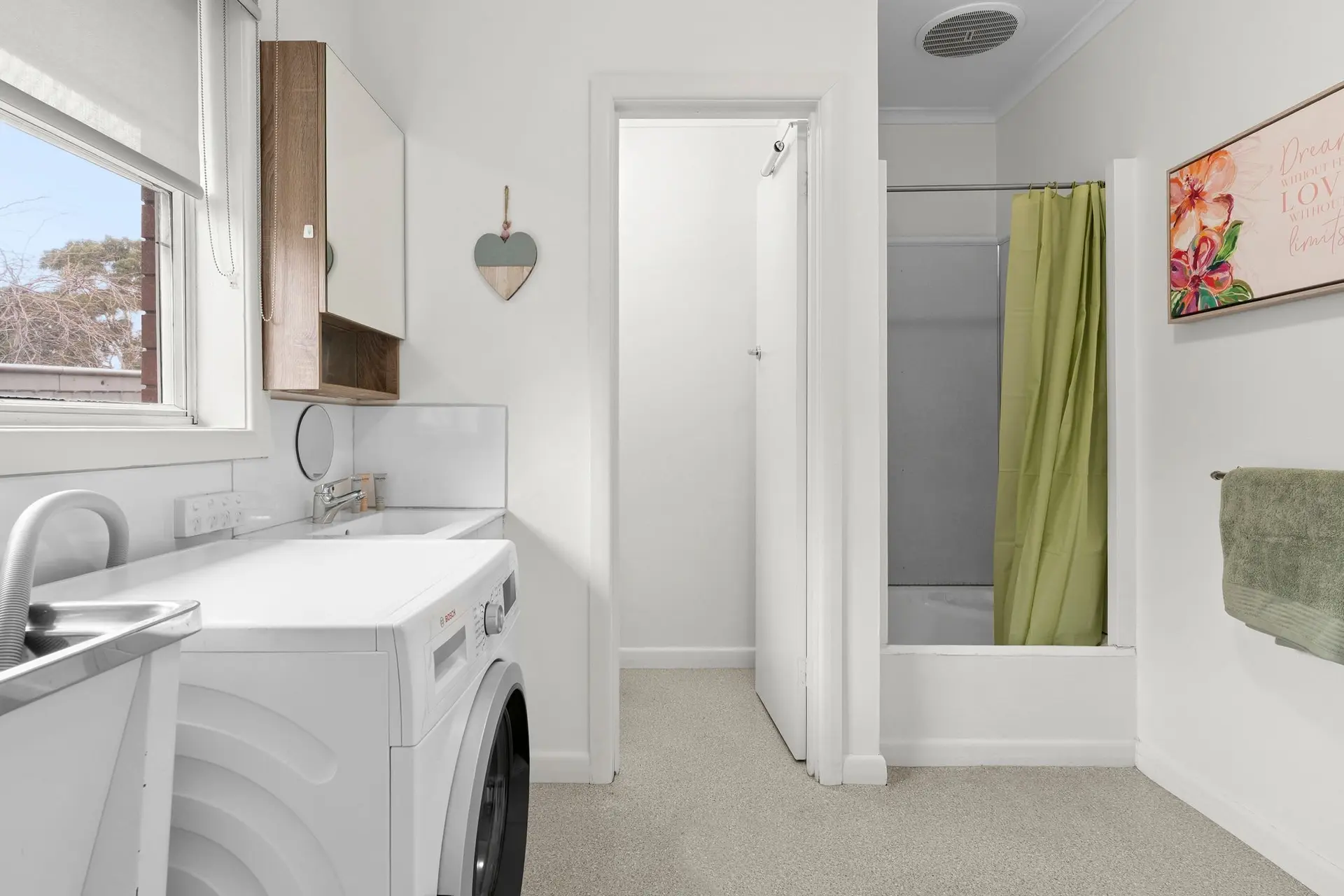 A laundry room with a washing machine, sink, and a hallway leading to a bathroom.