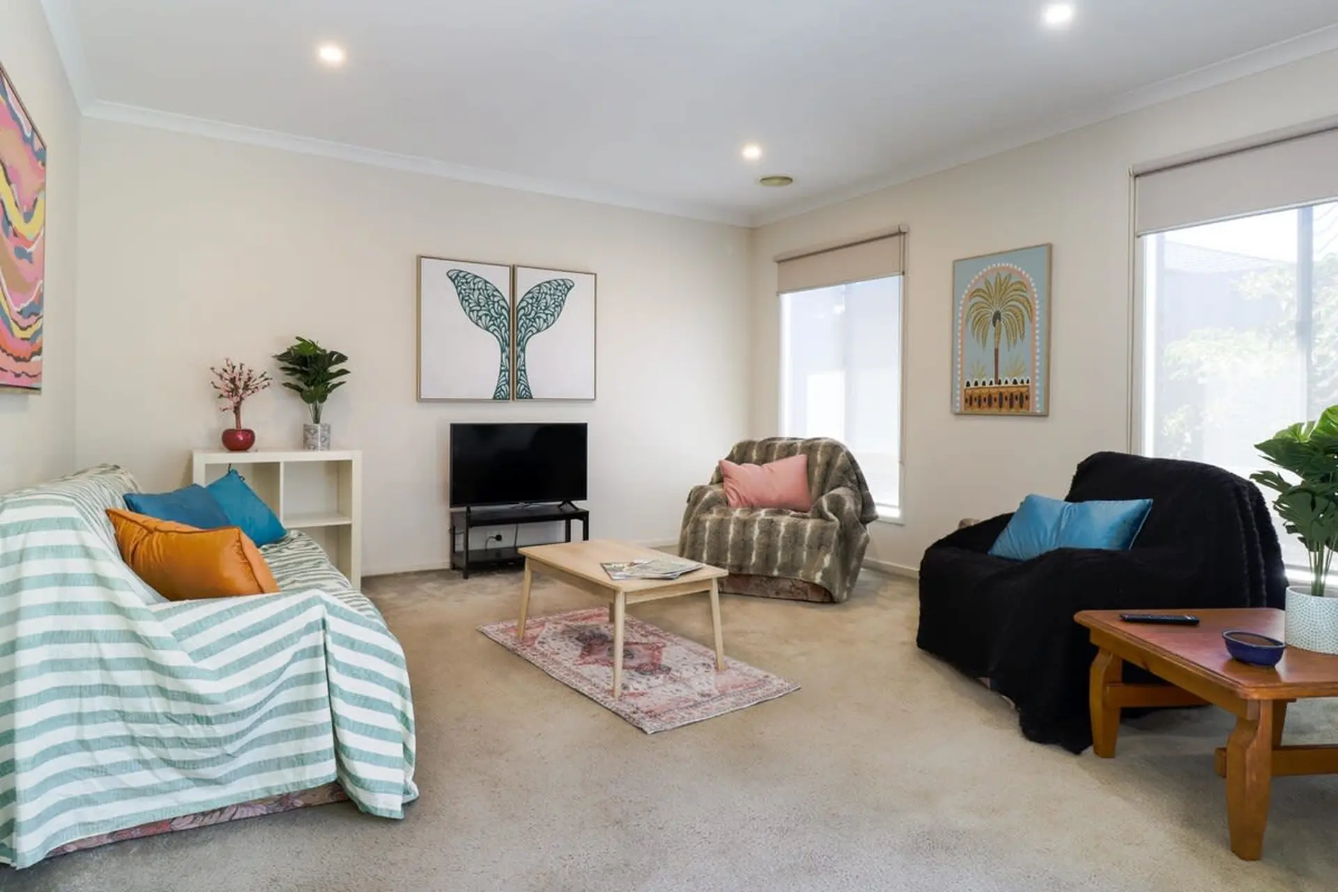 A well-lit living room with a sofa, armchairs, coffee table, and TV.