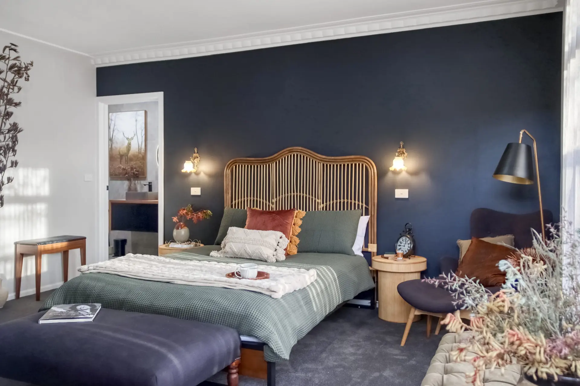 A bed with a dark green waffle weave comforter is in a bedroom with dark blue walls.