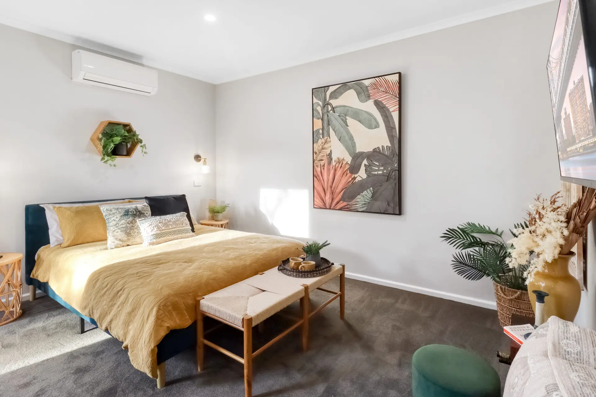 A bedroom with a yellow bed, botanical art, and a TV.