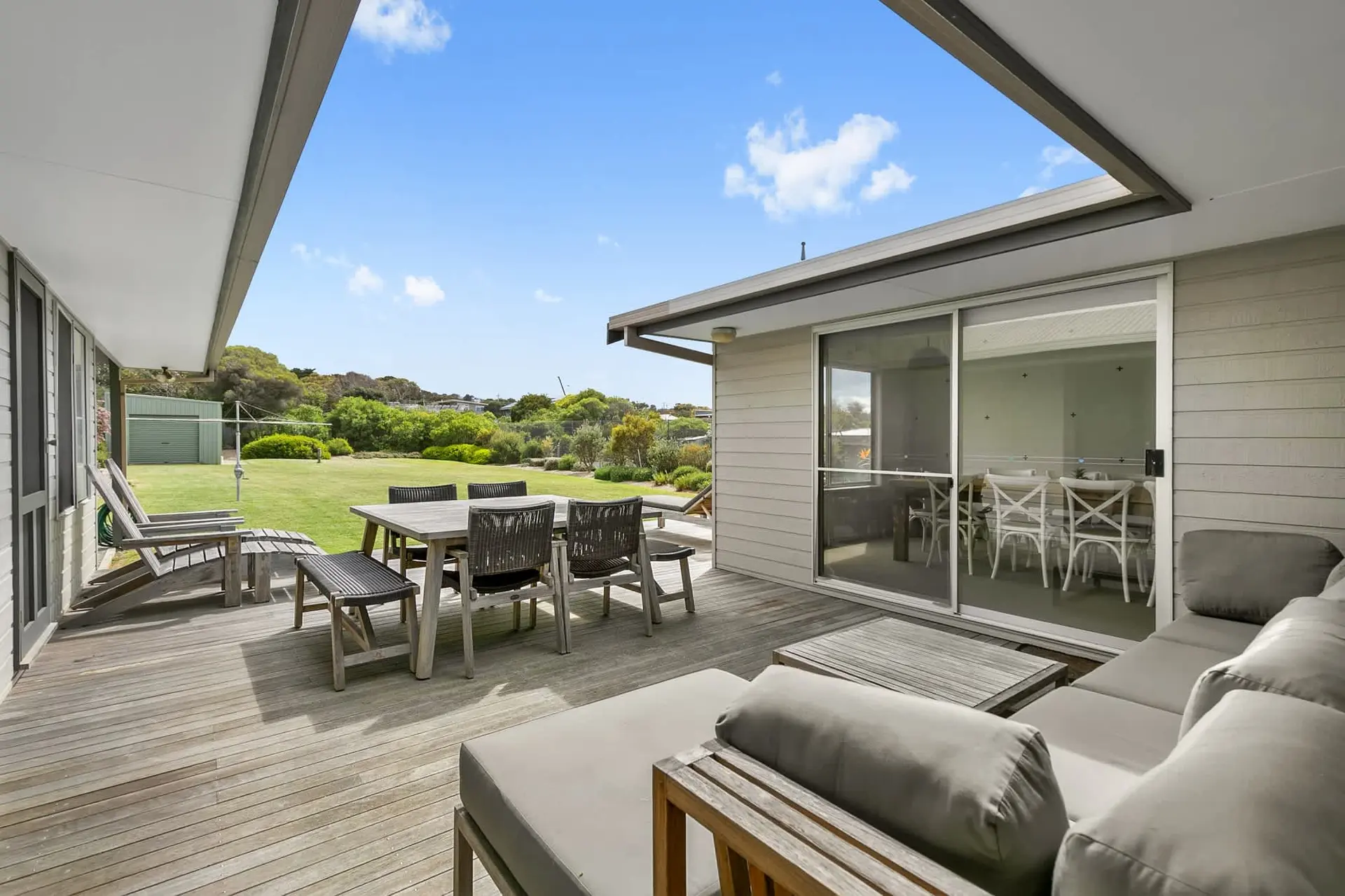 Outdoor deck with dining set, lounge furniture, and view of a grassy yard.