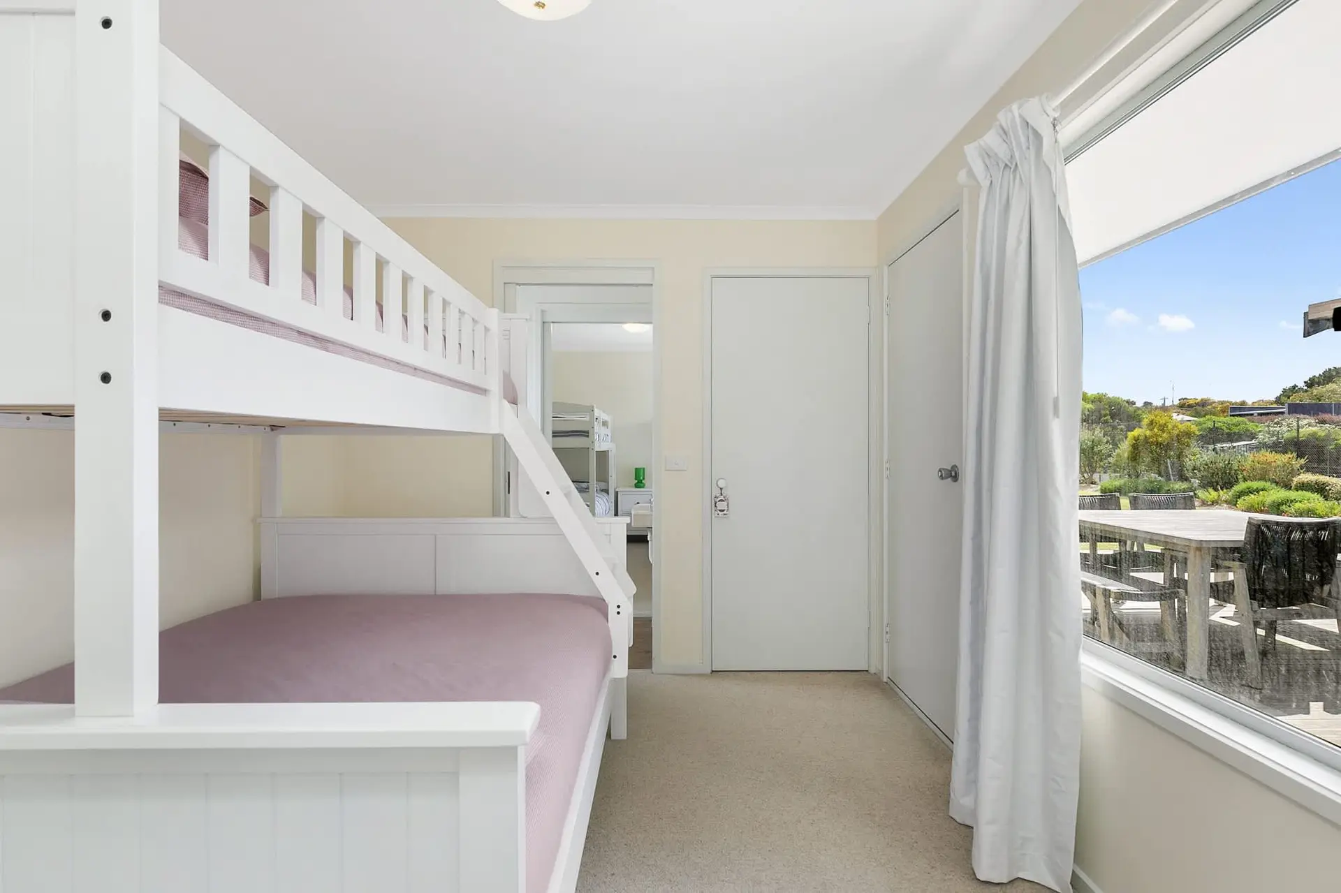 Bunk beds in a bedroom with a window view of a backyard dining area and landscape.