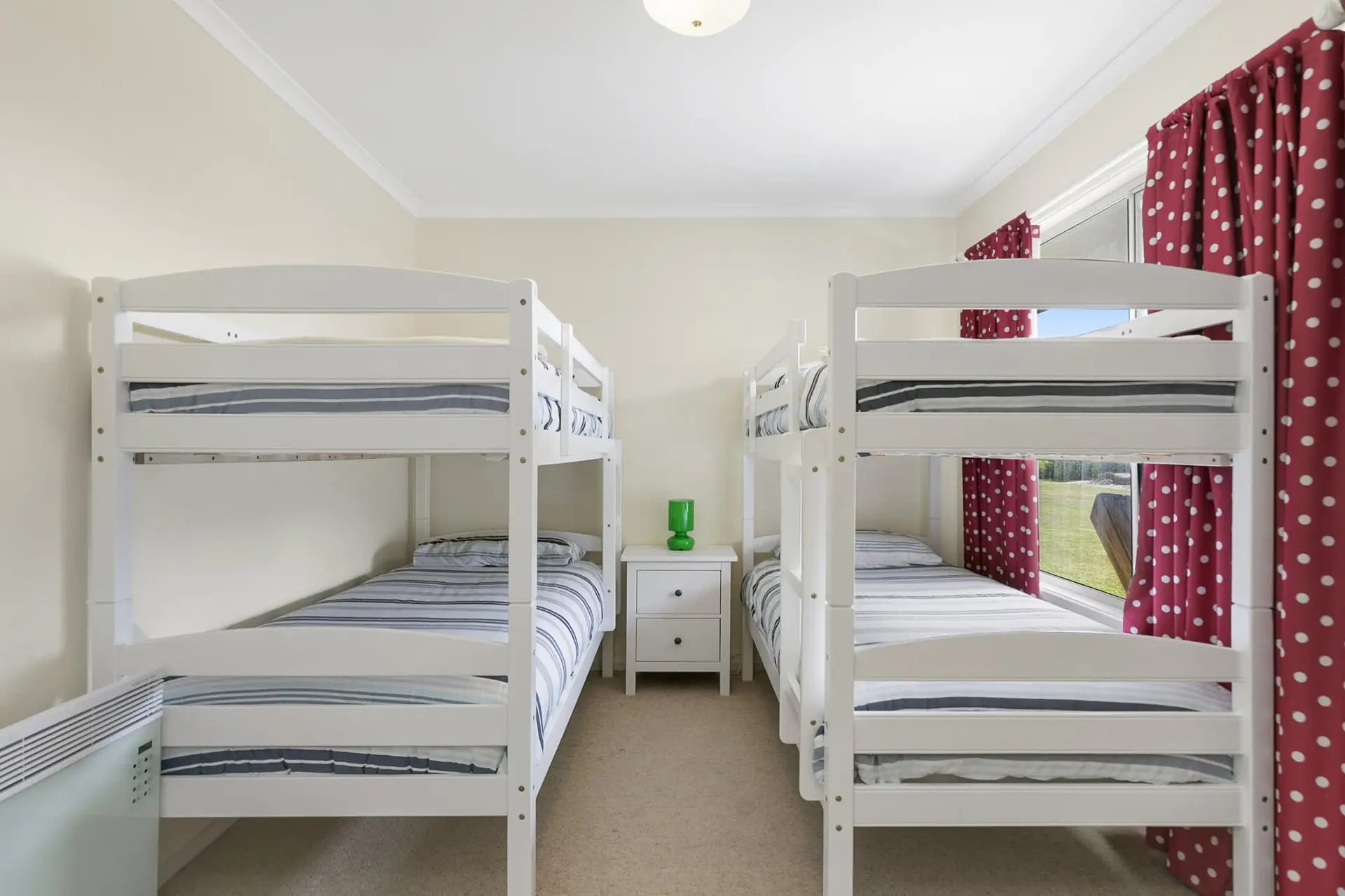A bedroom with two white bunk beds and red polka dot curtains.