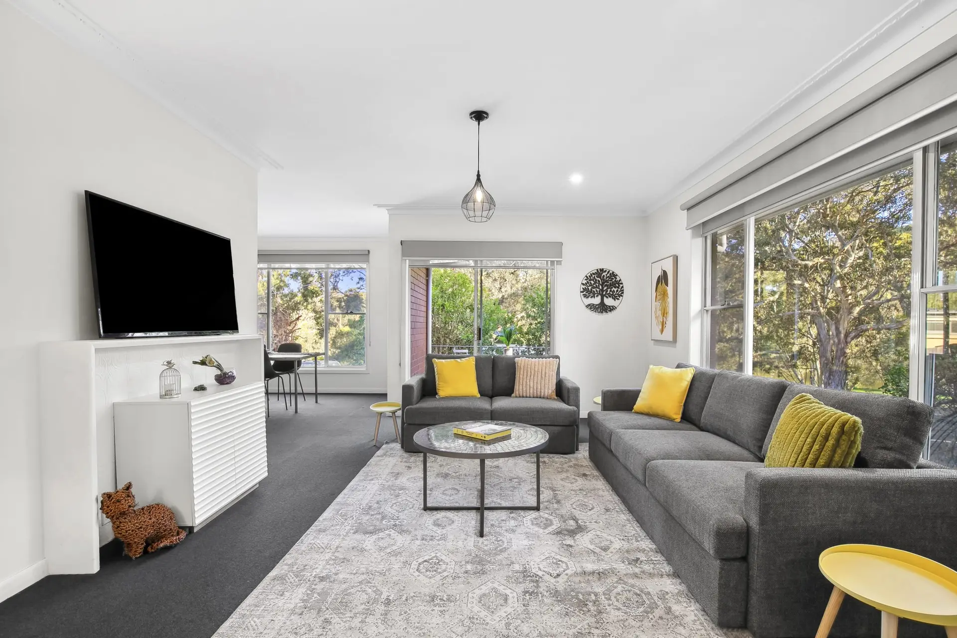 Living room with gray sectional sofa, yellow pillows, and a large window view of trees.