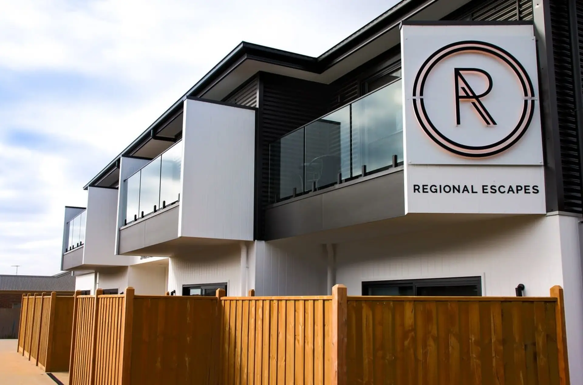 A modern building with balconies, a wooden fence, and a "Regional Escapes" sign.