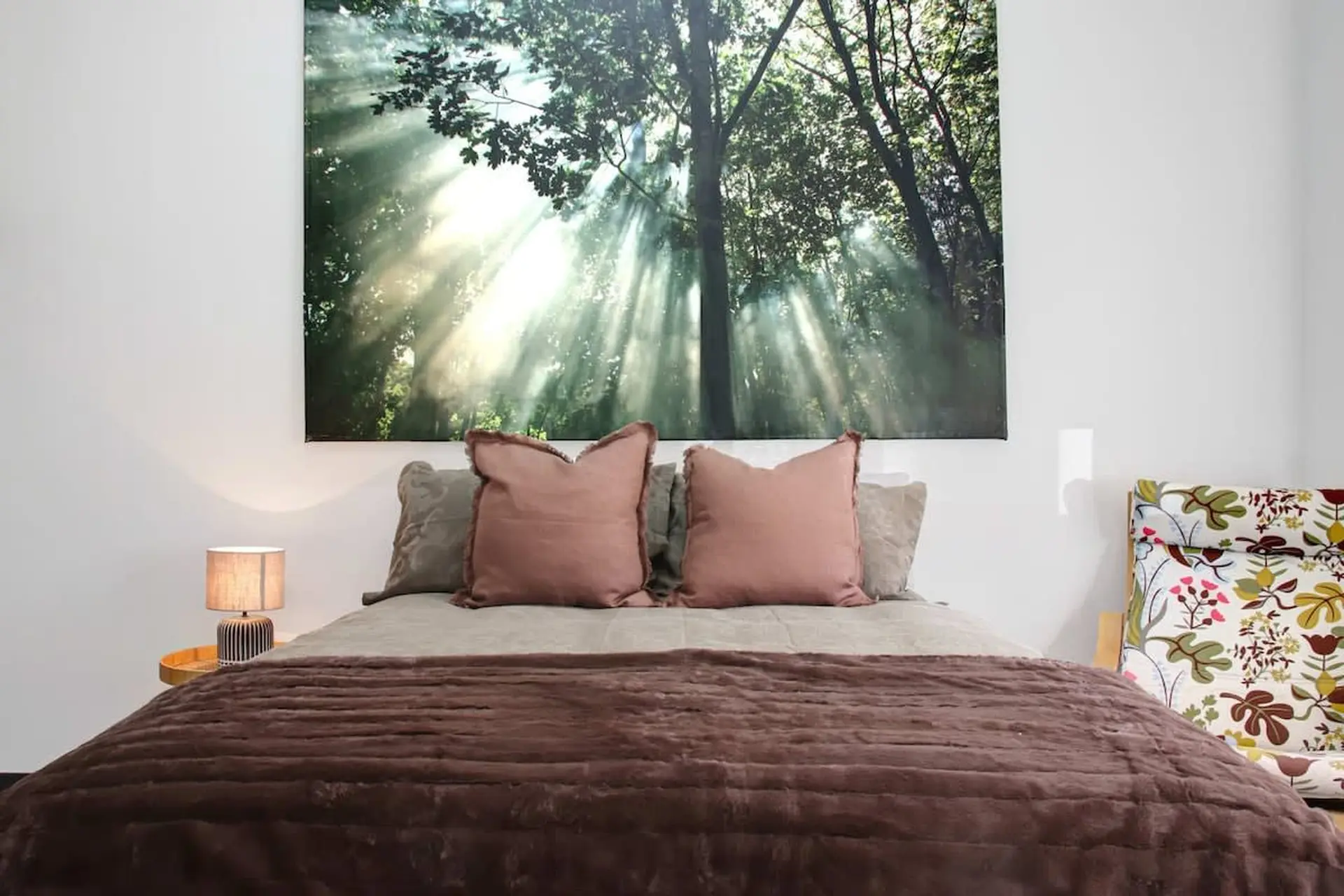 A cozy bedroom with a large forest mural and a plush brown blanket.