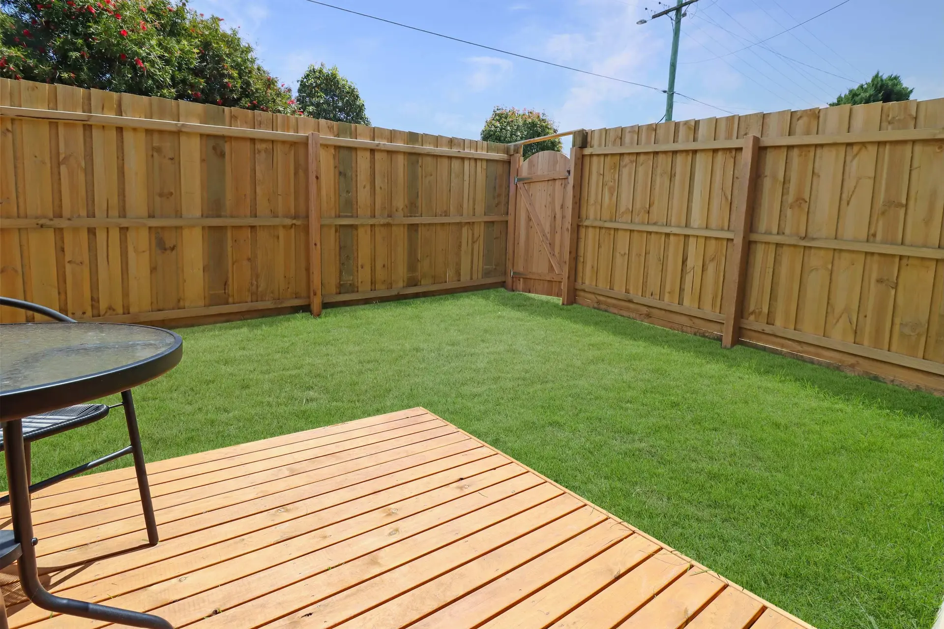 A wooden deck and a green lawn are in a fenced backyard.