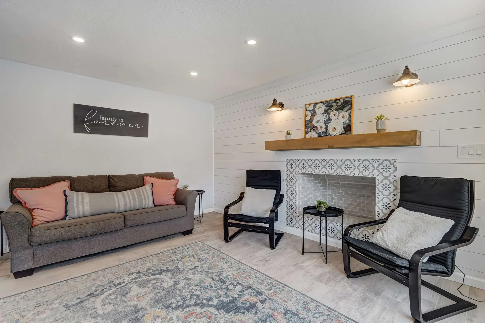 A modern living room with a gray sofa, shiplap walls, tiled fireplace, and two armchairs.