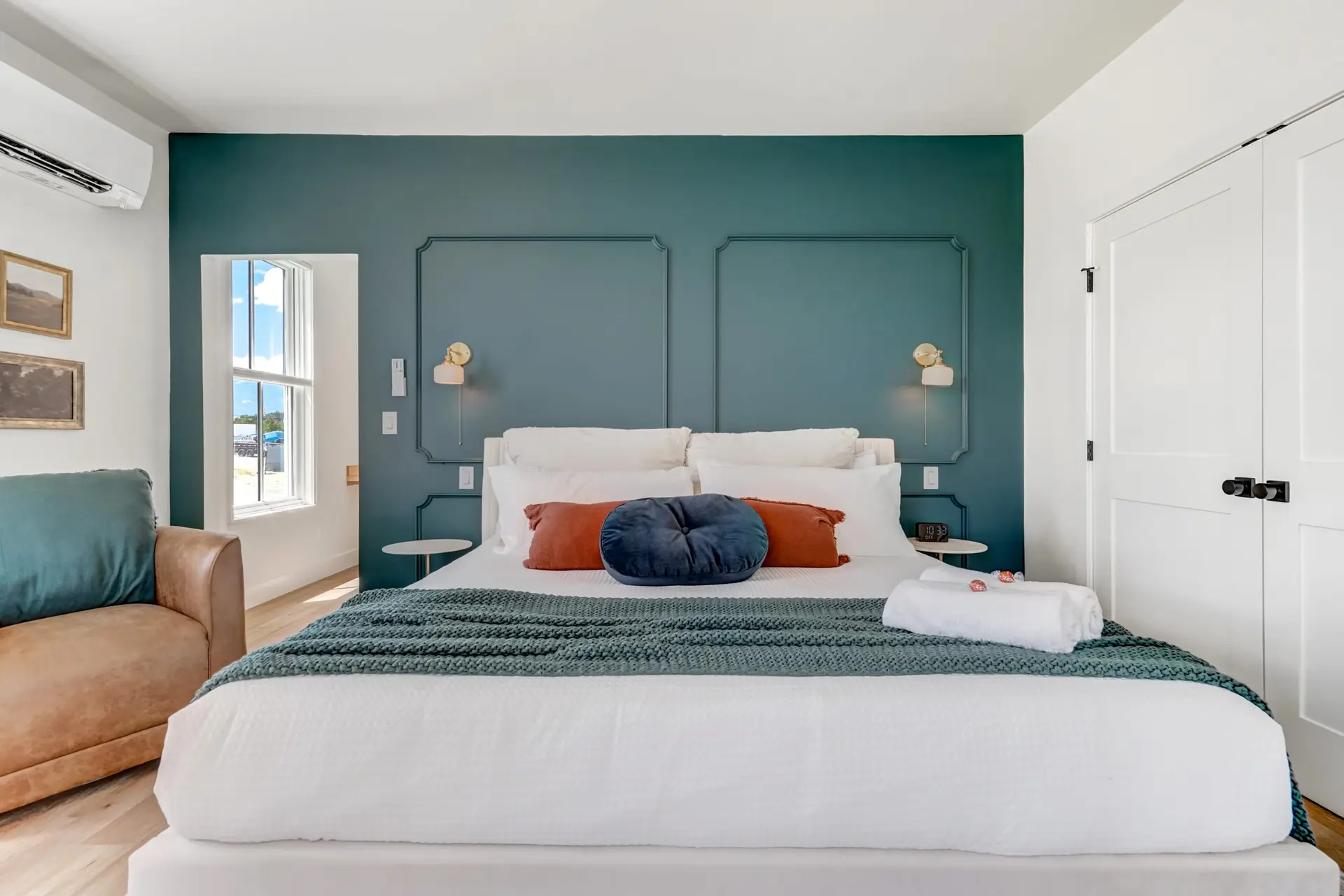 Full view of a modern bedroom with a large bed, teal accent wall, window, and white closet.
