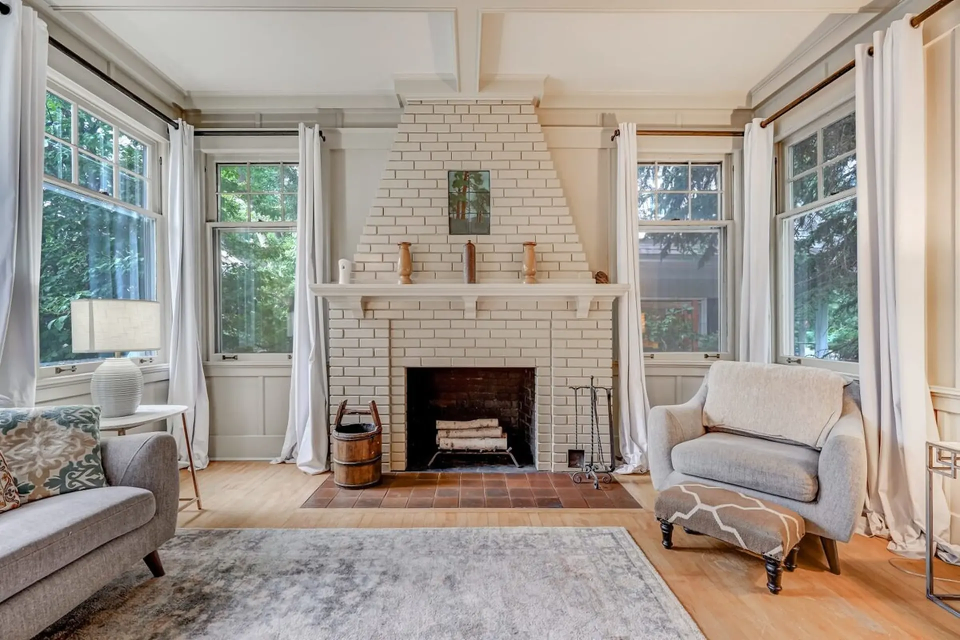 Living room with white brick fireplace, gray sofa, armchair, and windows providing natural light.