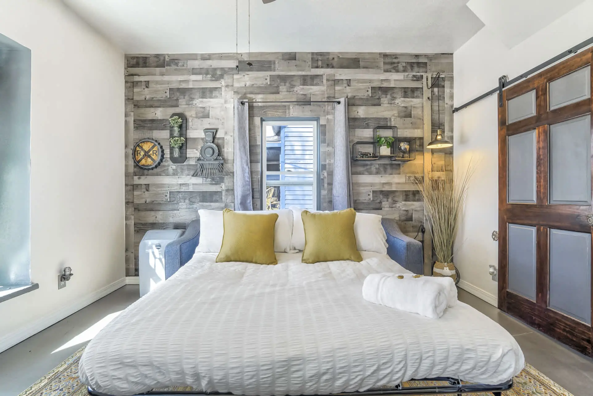 A bed with white bedding and yellow pillows is in a room with a rustic wooden wall.