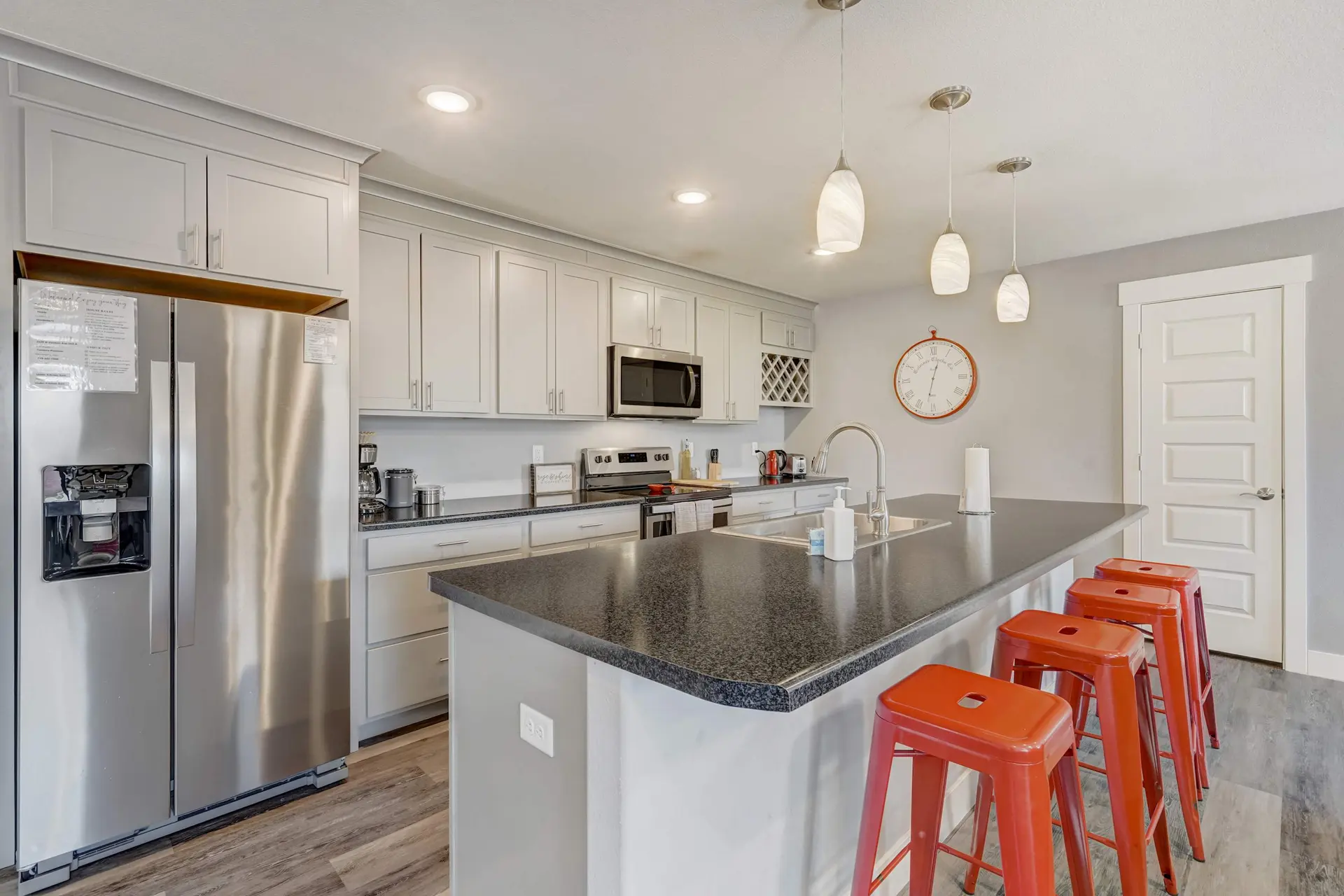A modern kitchen featuring light grey cabinets, dark counters, stainless steel appliances, and orang