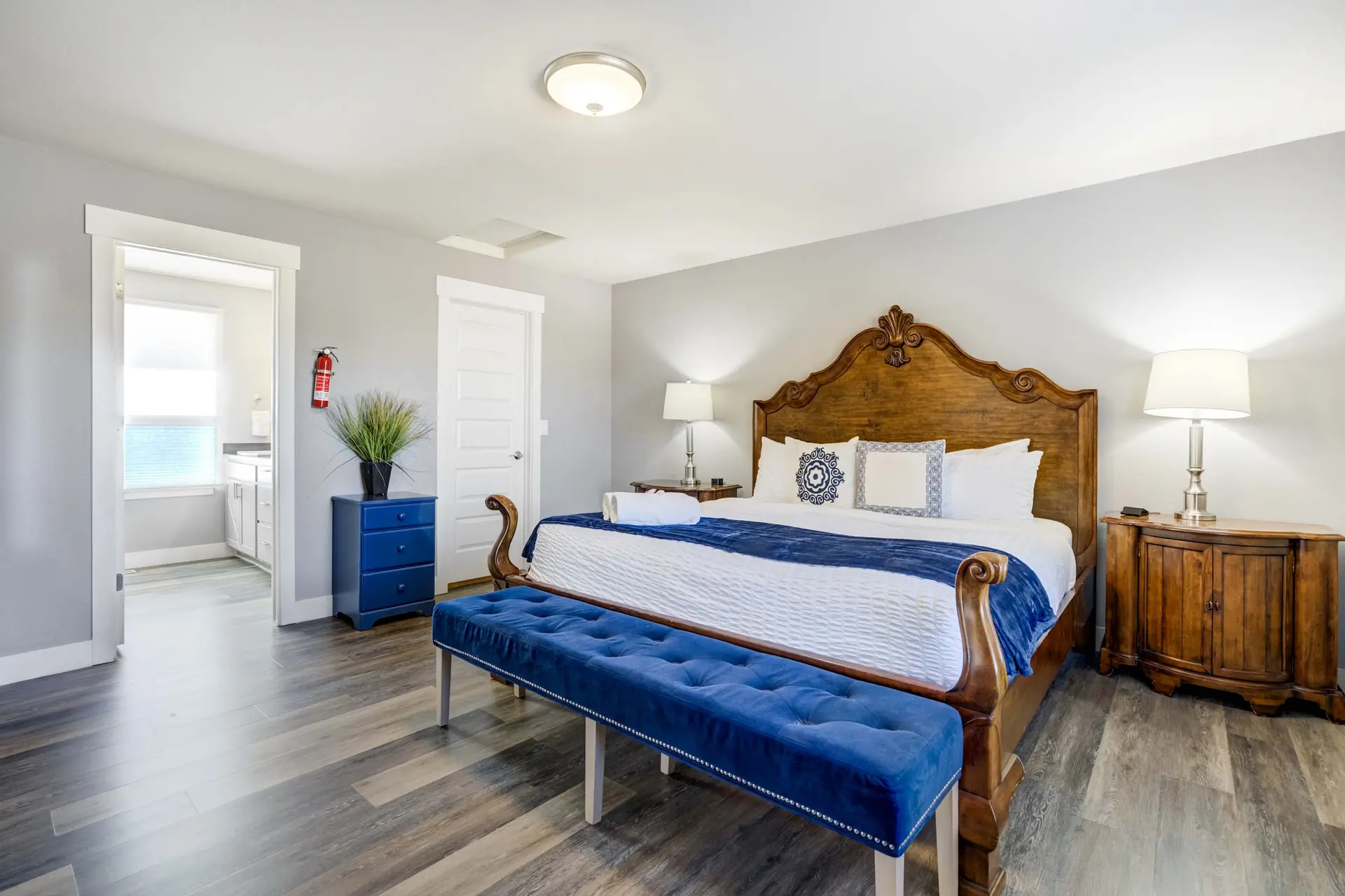 A spacious bedroom with a king-sized wooden bed, blue and white linens, a blue tufted bench, and two