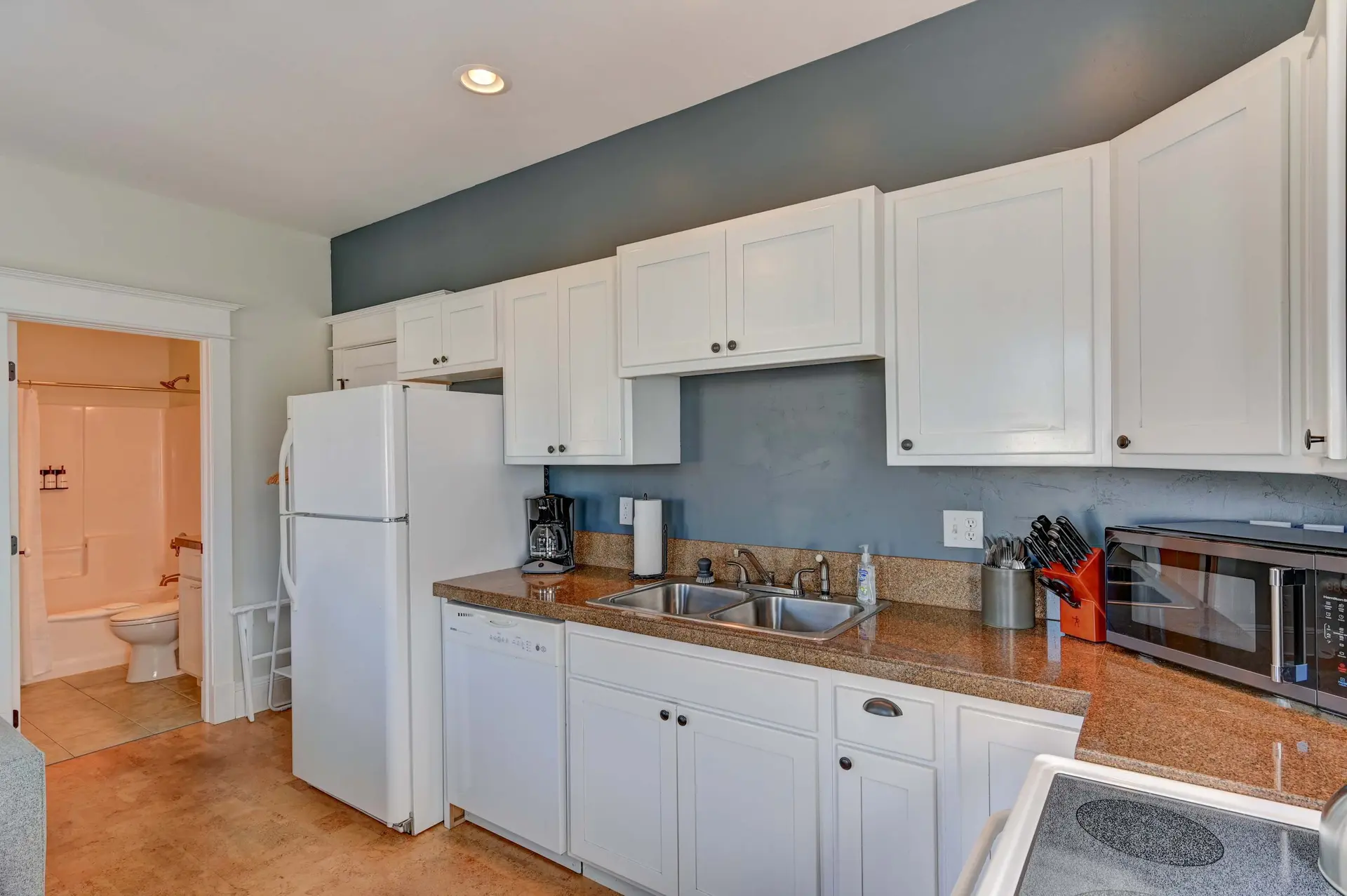 A white kitchen with a blue accent wall and speckled granite countertops.