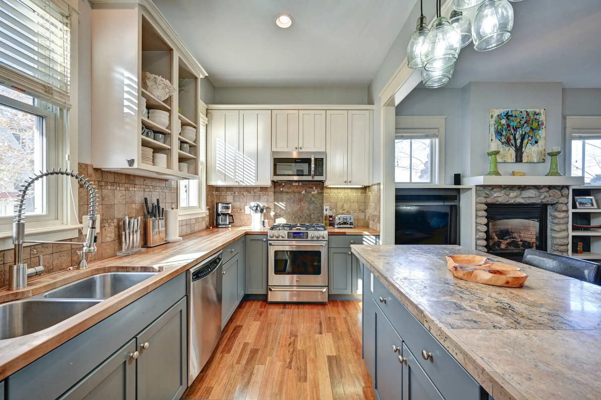 A modern kitchen with a granite island, stainless steel appliances, and a stone fireplace.