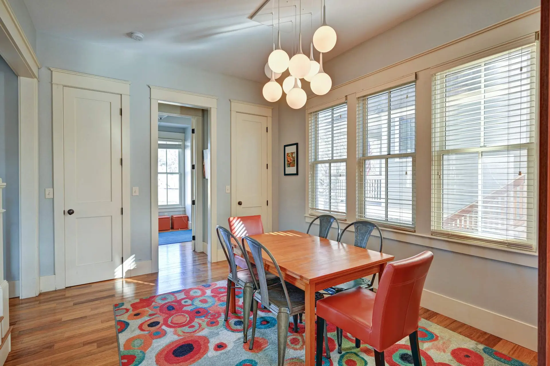 A dining room with a wooden table and chairs is in front of a wall with three windows.
