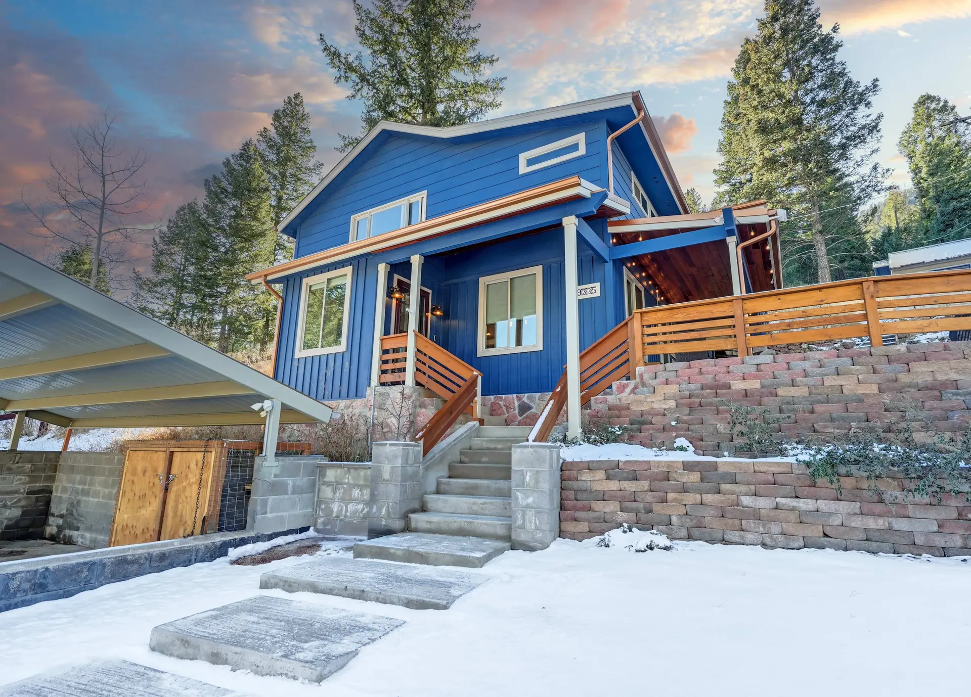 A bright blue house with a wooden deck in a snowy landscape.