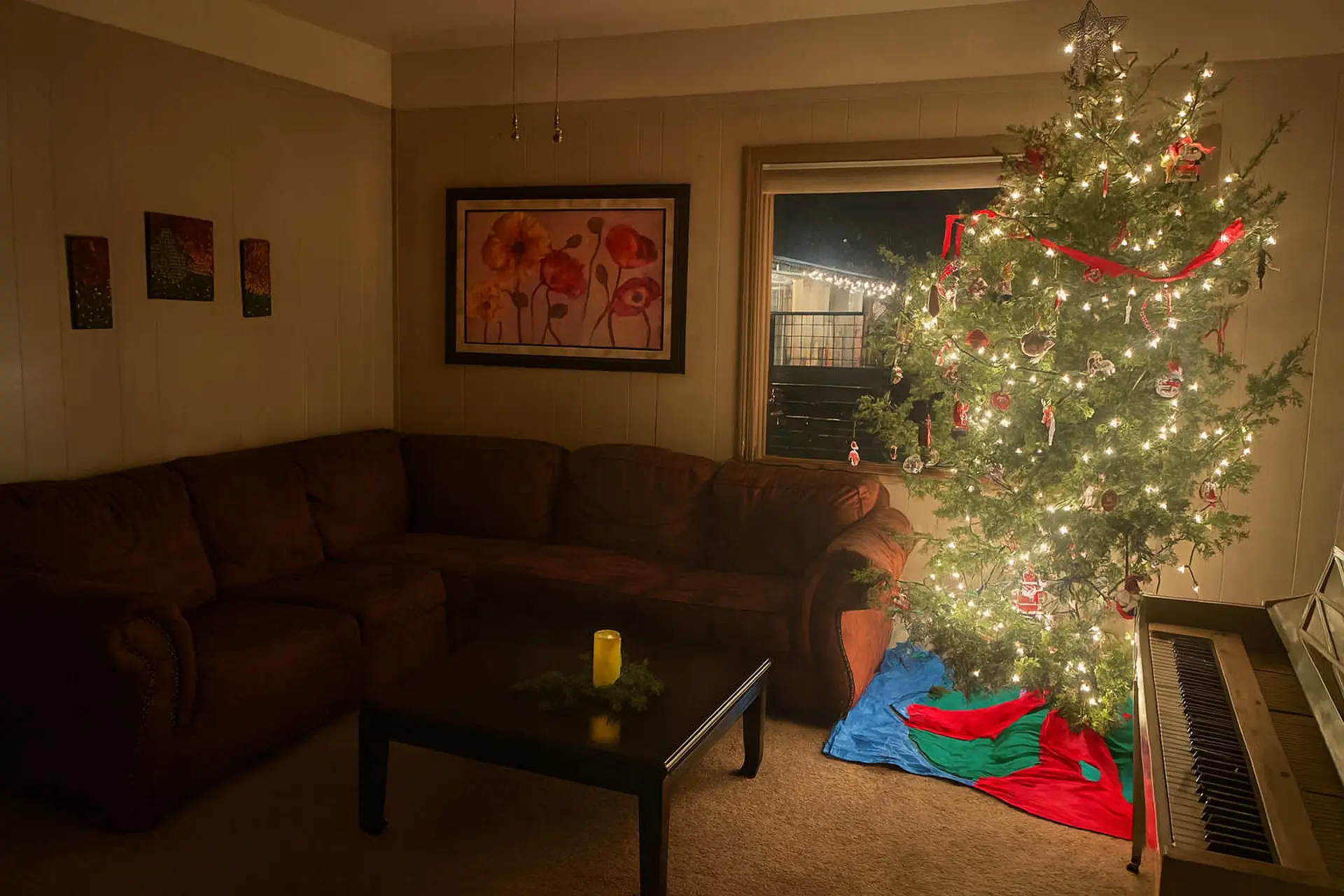 A decorated Christmas tree with lights and ornaments stands next to a piano in a dimly lit living ro