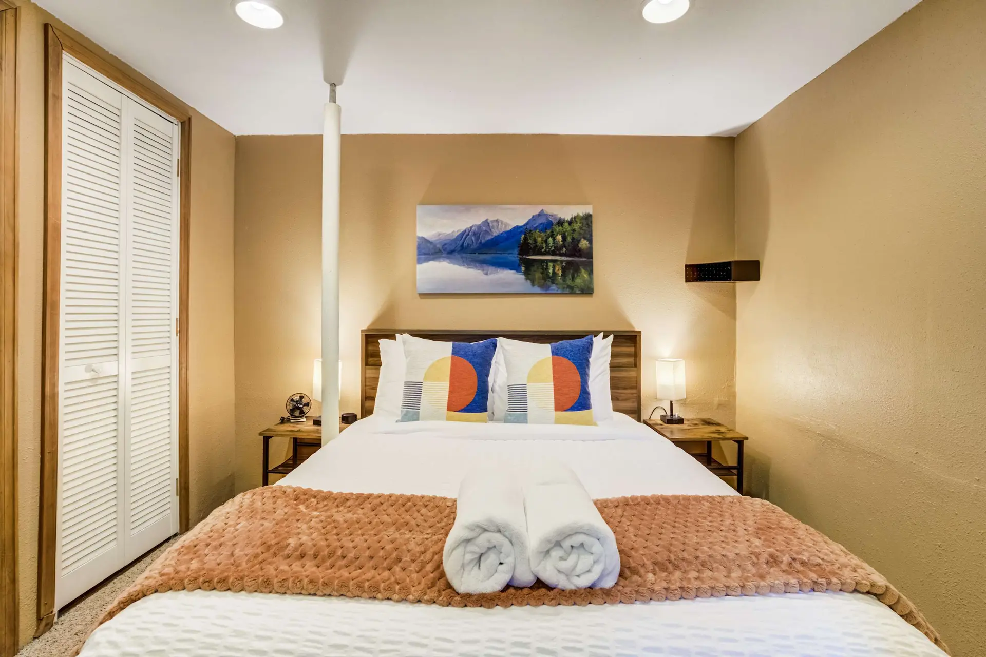Bedroom with a bed, two pillows with geometric patterns, and a landscape painting on the wall.