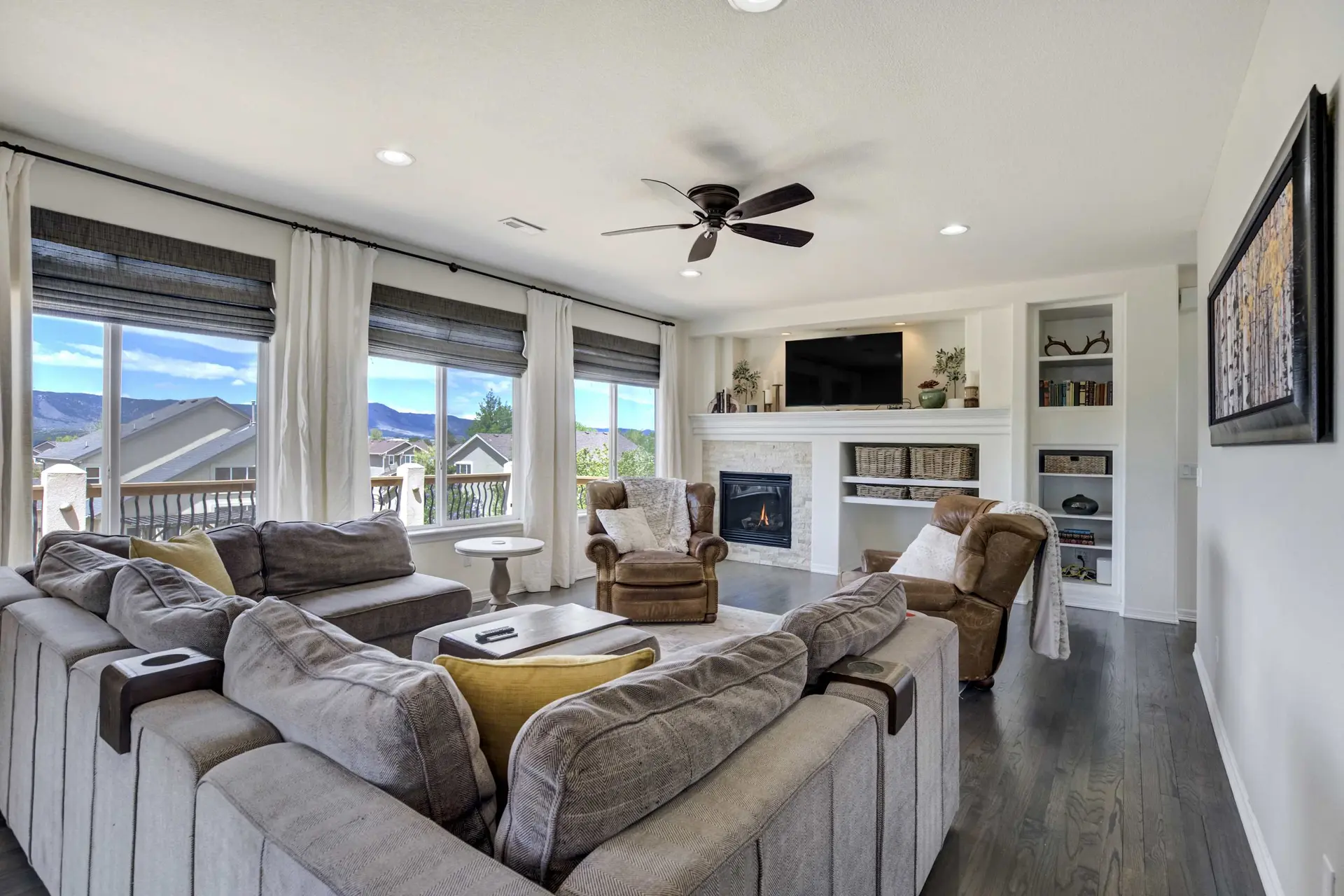 A spacious living room with a large gray sectional, fireplace, TV, and mountain views from windows.