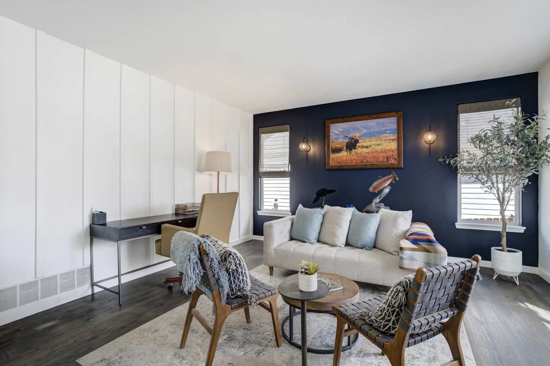 A stylish living room with dark blue and white shiplap walls, a desk, sofa, two chairs, and artwork.