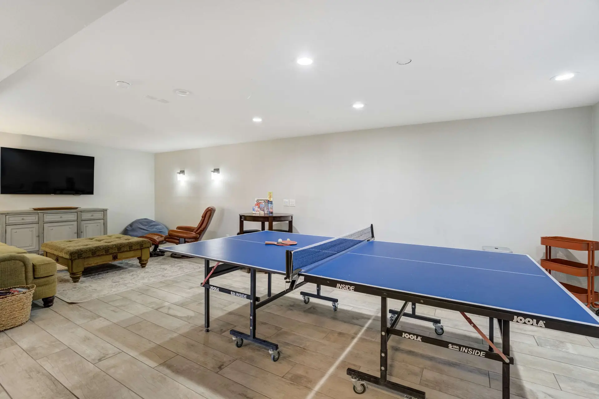 Spacious basement game room with a JOOLA ping-pong table, TV, and comfortable seating areas.