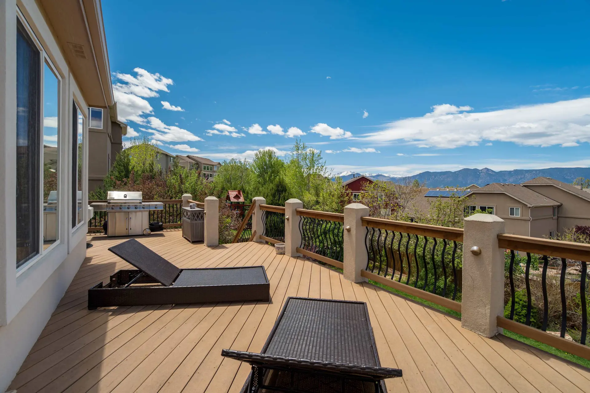 Expansive wooden deck with lounge chairs, grill, and fire pit, overlooking houses, trees, and mounta