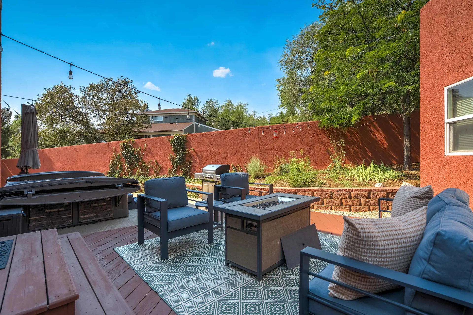 A vibrant backyard patio featuring outdoor seating, a fire pit, grill, and hot tub against a red wal
