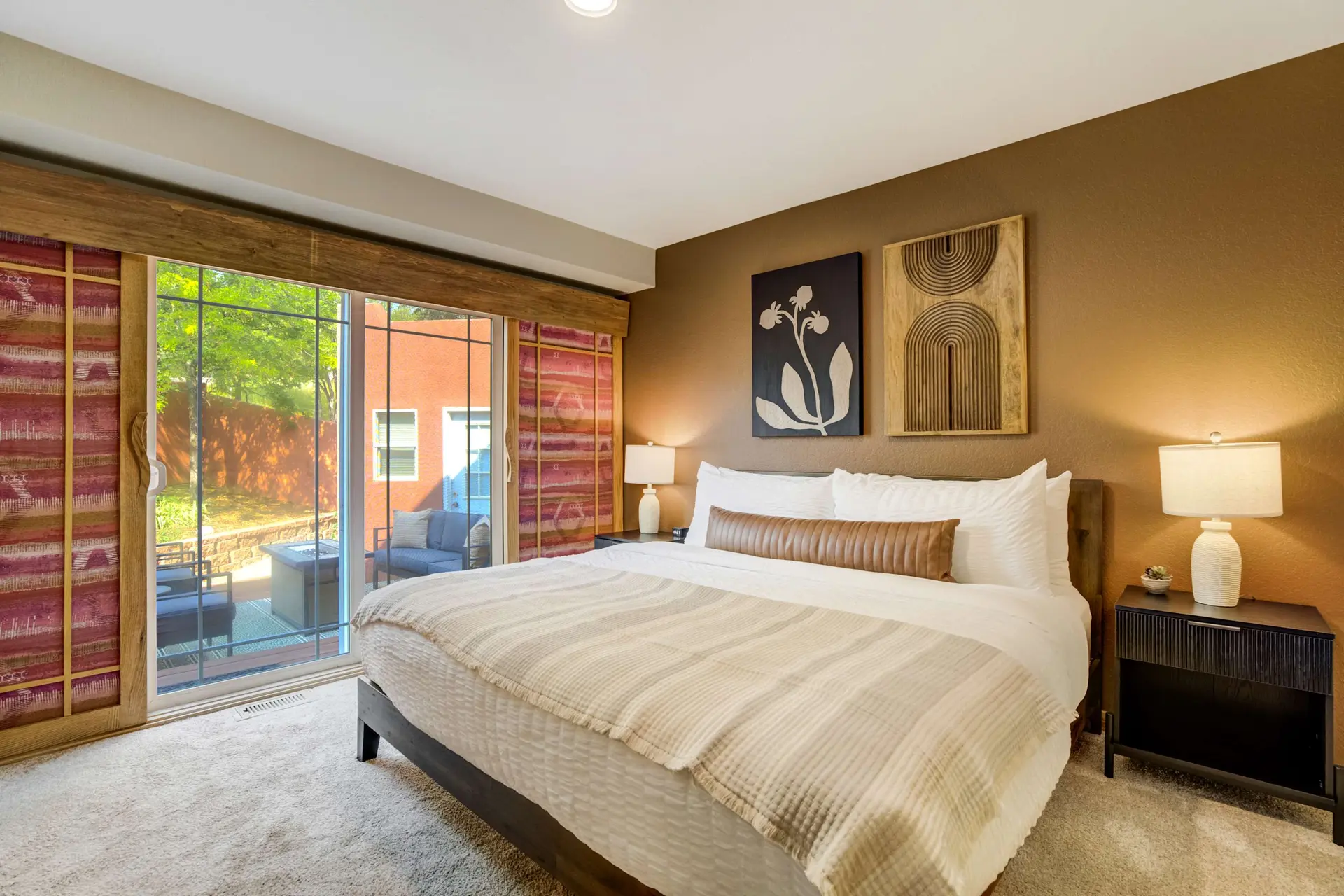A warm bedroom with a king-size bed, brown walls, art, and a sliding glass door to a patio.
