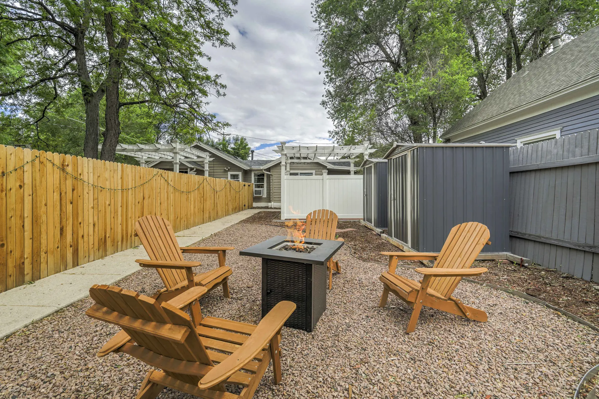 Backyard with fire pit, adirondack chairs, and wooden fence.